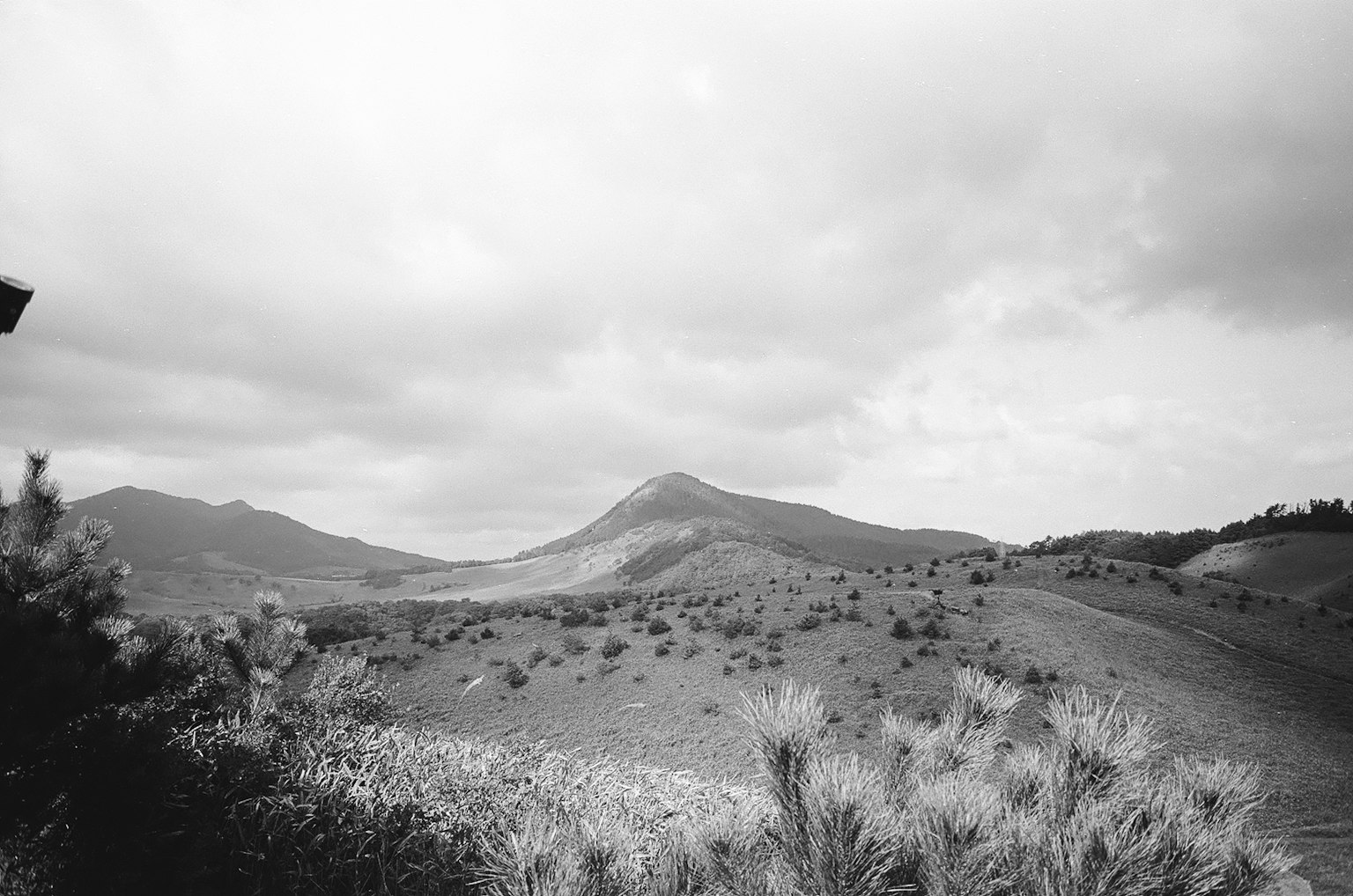 黑白風景照片，顯示丘陵和山脈，雲層密布的天空