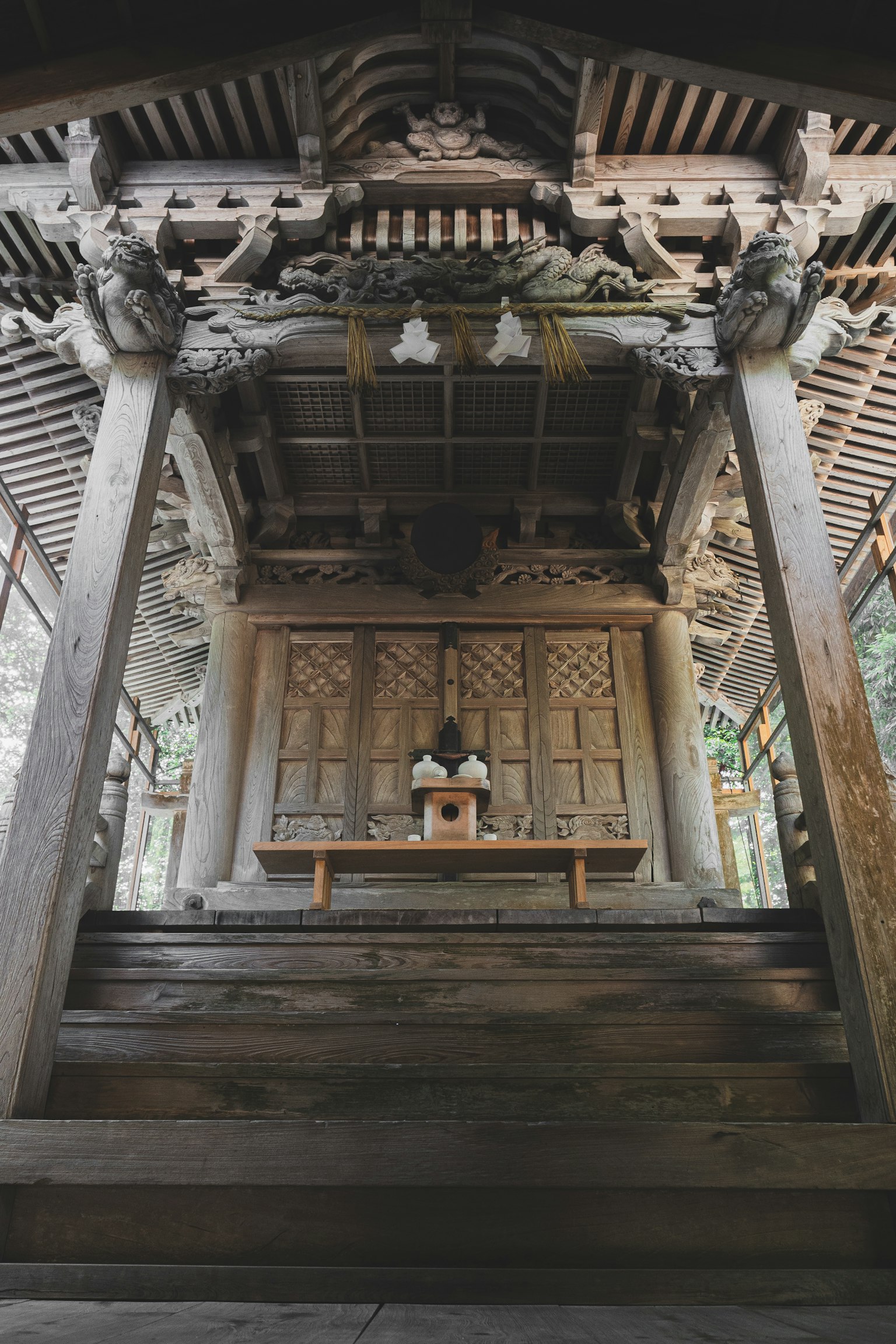 Vista interna di un santuario in legno tradizionale con intricate sculture e un altare in cima alle scale