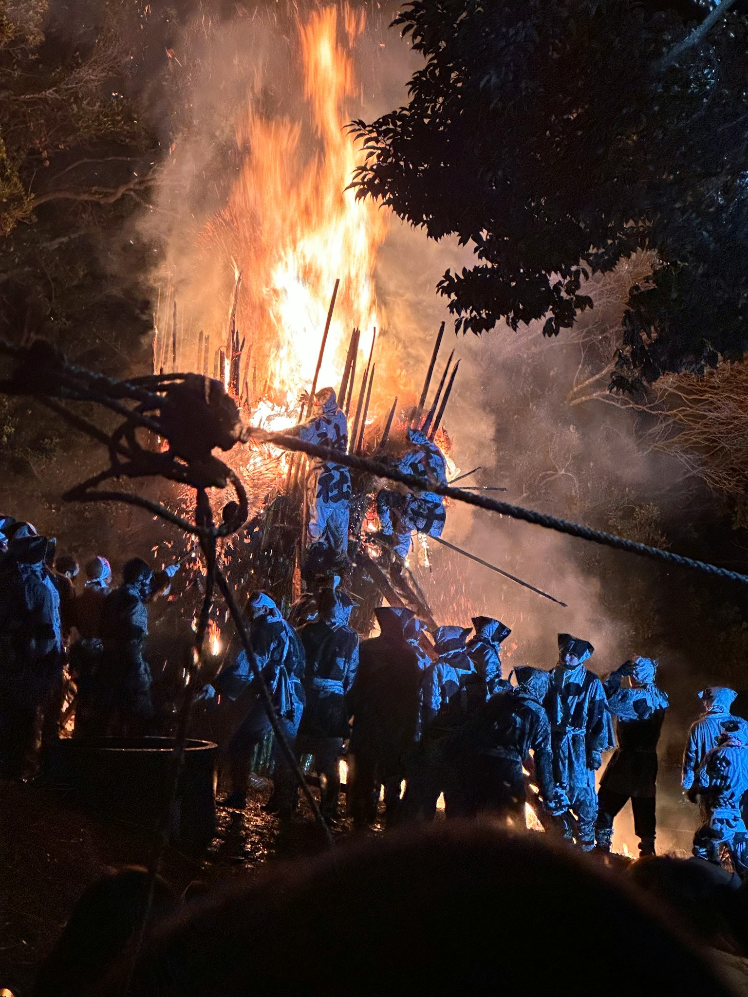 Una escena de festival nocturno con personas vestidas de azul reunidas alrededor de un gran fuego
