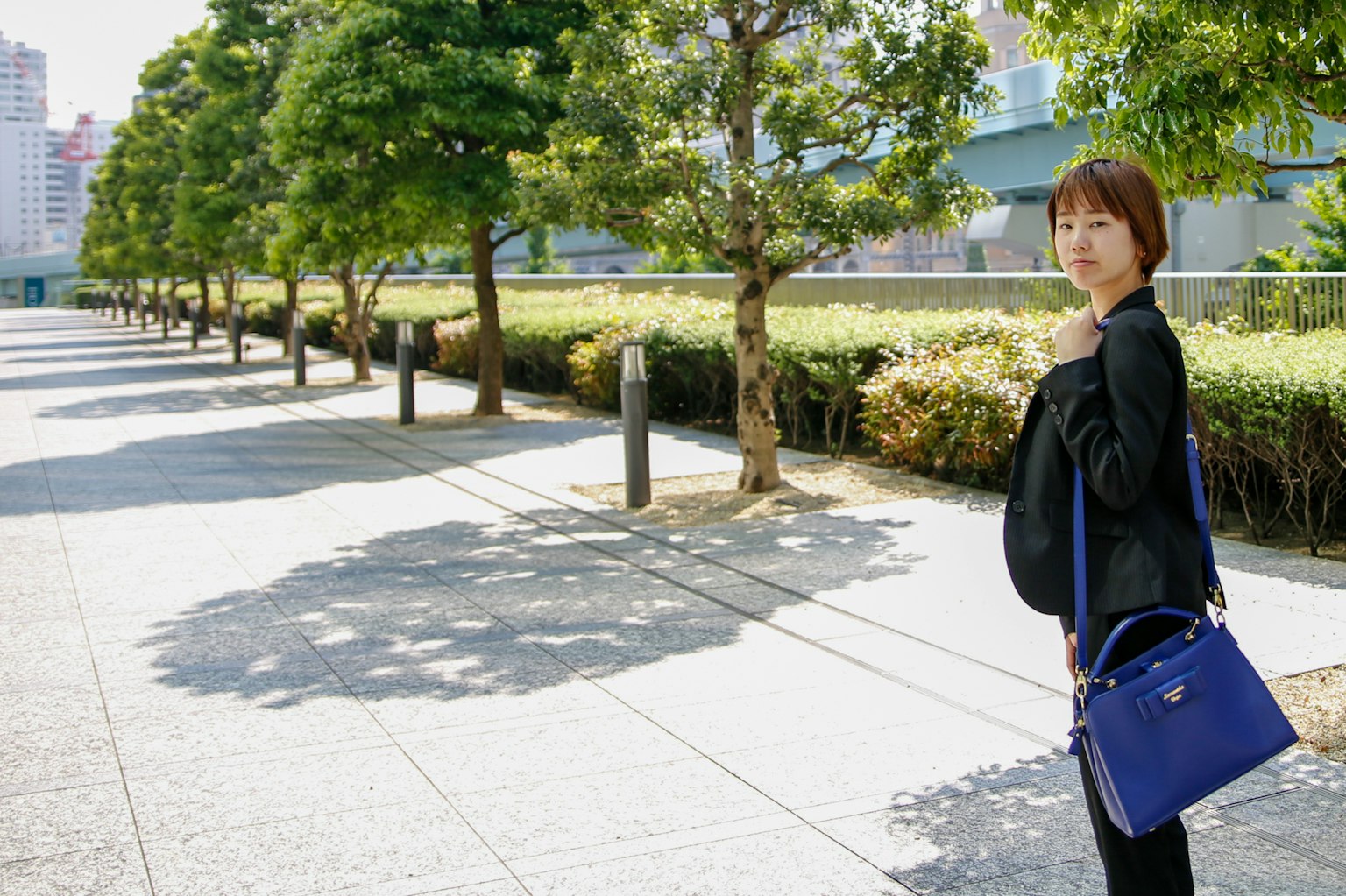一位女性正在公園小路上走，手裡拿著一個藍色的包