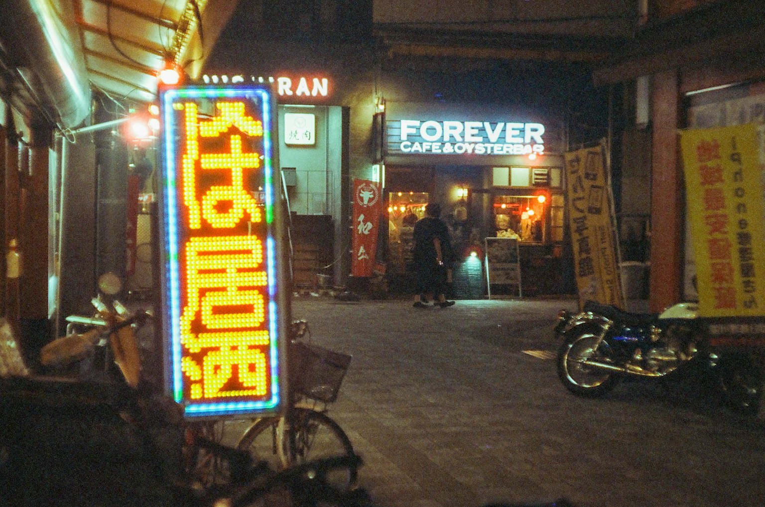 Scena notturna di strada con insegne al neon e un ristorante