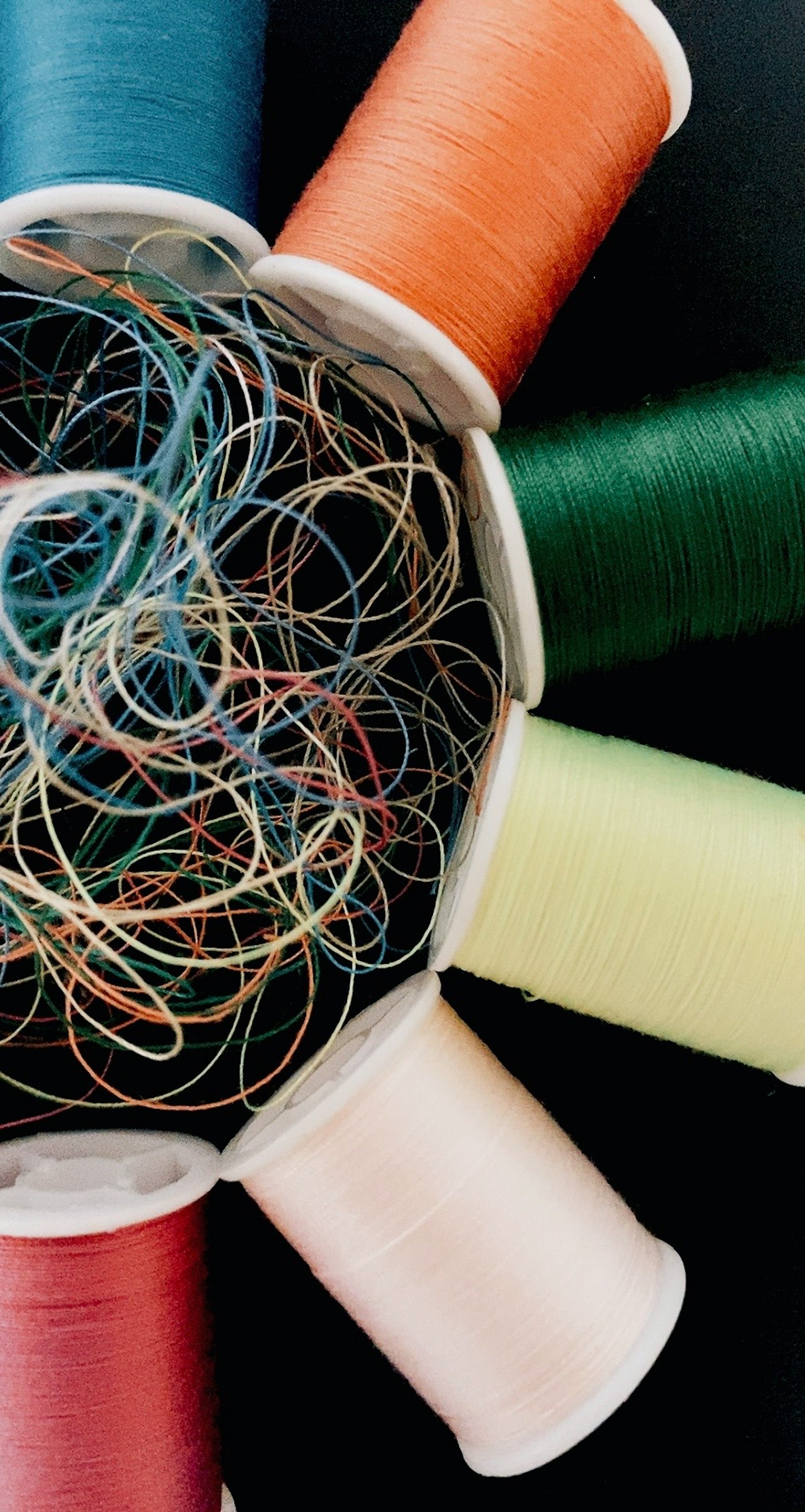 Bunte Garnrollen, die um eine Schüssel mit verhedderten Gummibändern angeordnet sind