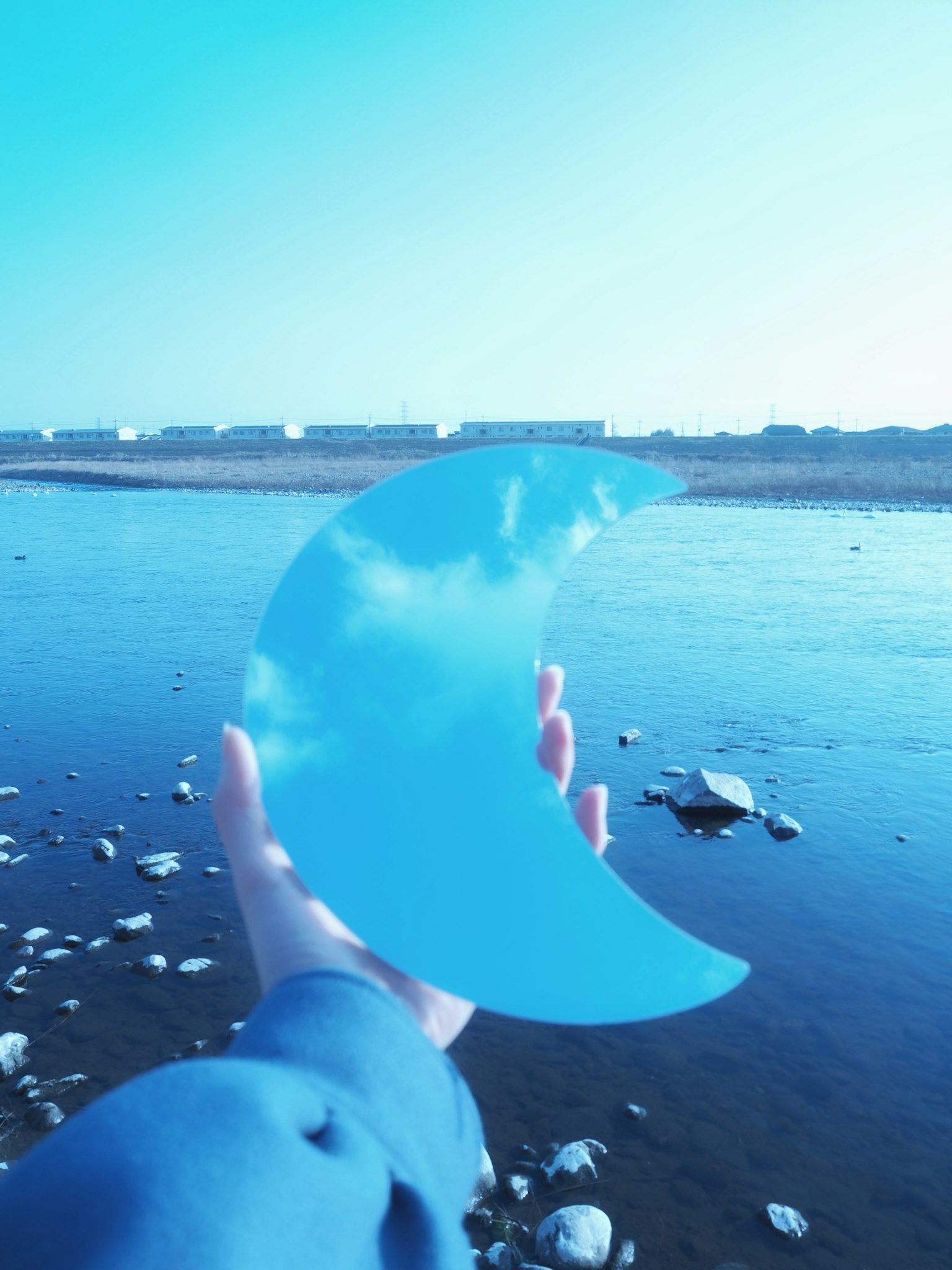 Mano che tiene un oggetto trasparente a forma di mezzaluna blu con sfondo di fiume