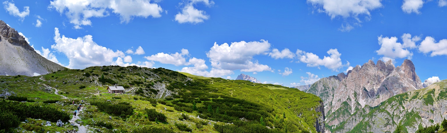 Pemandangan pegunungan dengan langit biru dan awan putih rumput hijau subur dan gunung berbatu curam