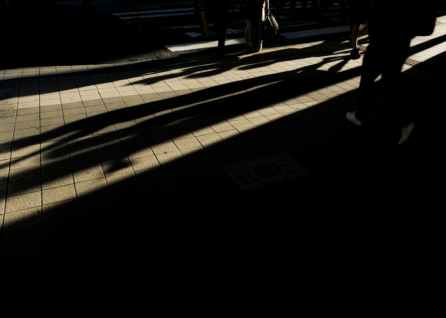 Silouette di persone che camminano proiettate nell'ombra su un marciapiede di città