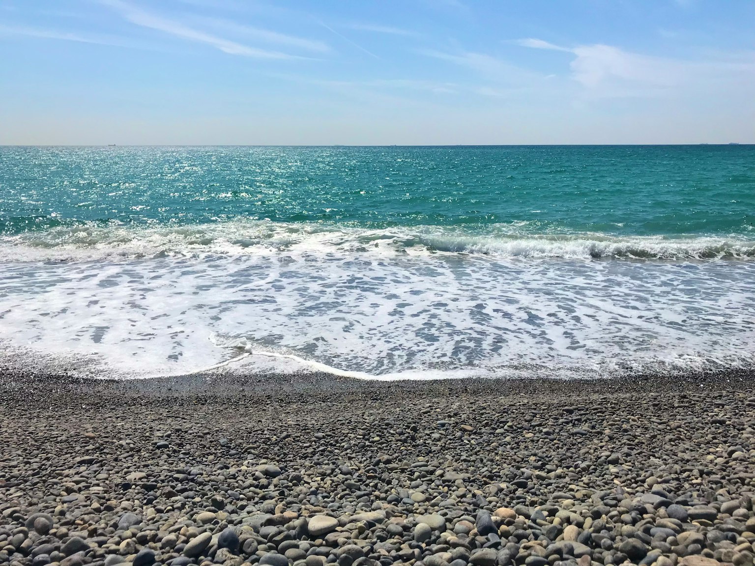 Pemandangan indah pantai berbatu dengan air turquoise dan gelombang lembut
