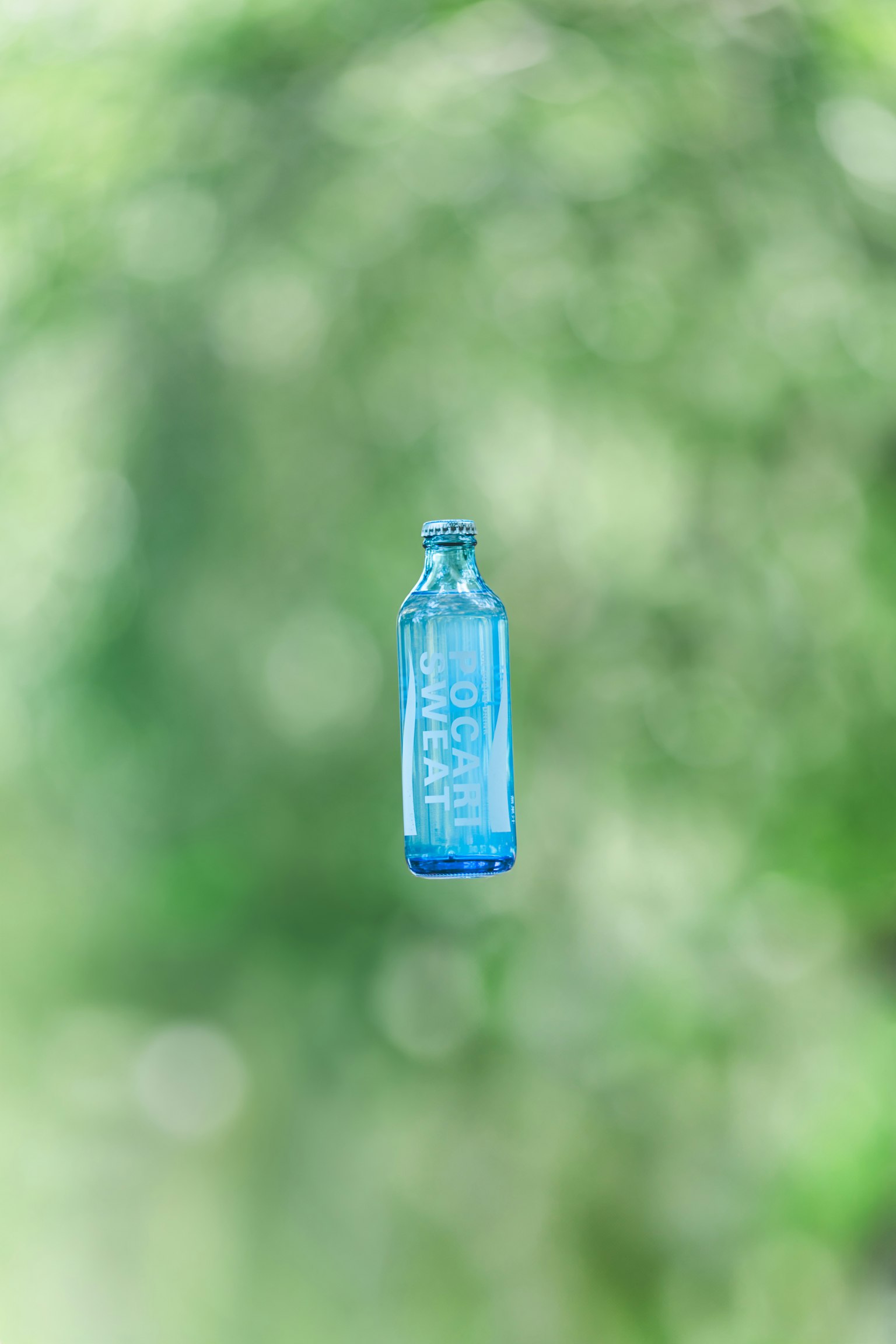 Eine transparente blaue Flasche, die vor einem verschwommenen grünen Hintergrund schwebt