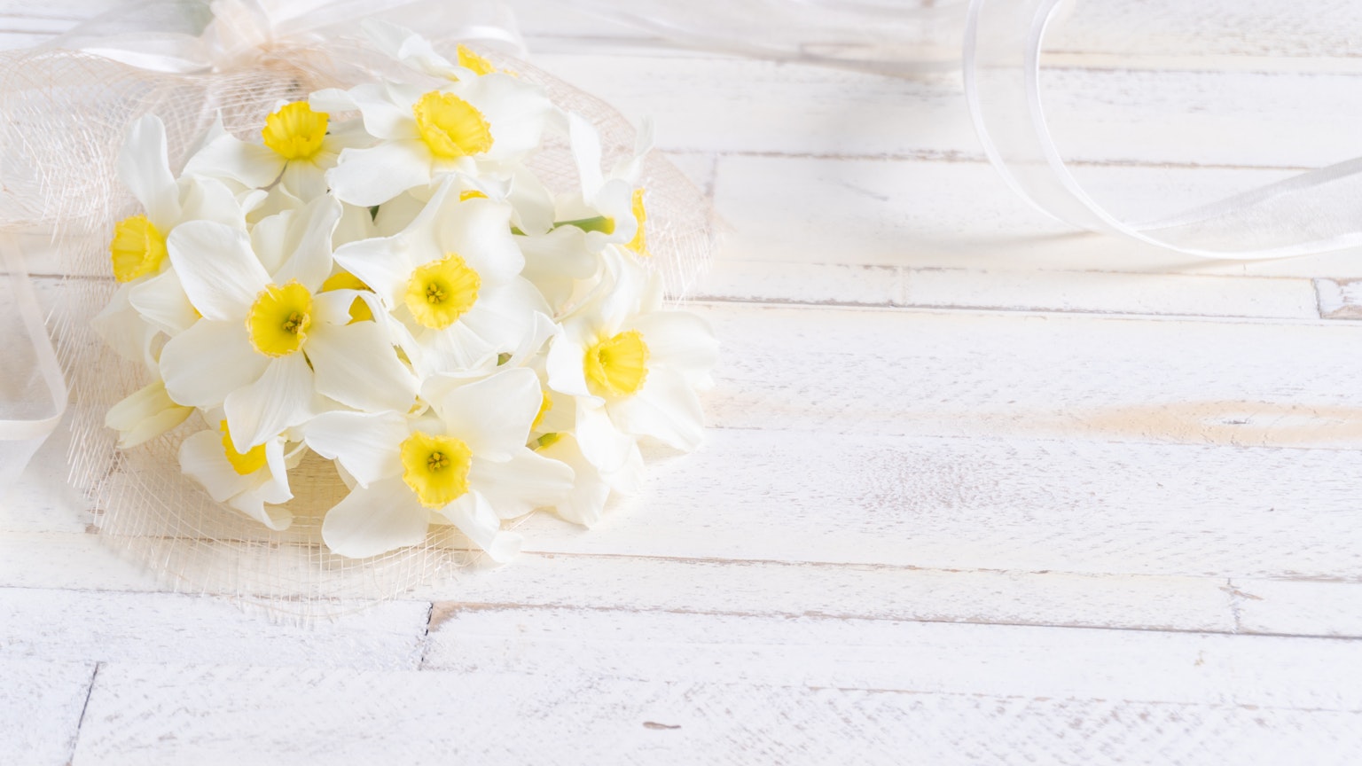 Un ramo de flores blancas con centros amarillos colocado sobre una mesa de madera blanca