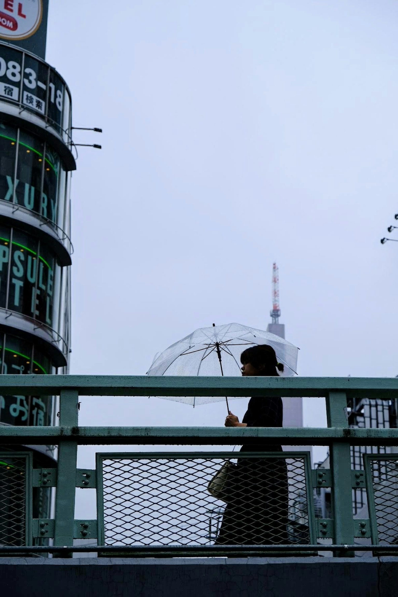 Silhouette của một người phụ nữ đi bộ với ô trong mưa với Tháp Tokyo ở phía sau