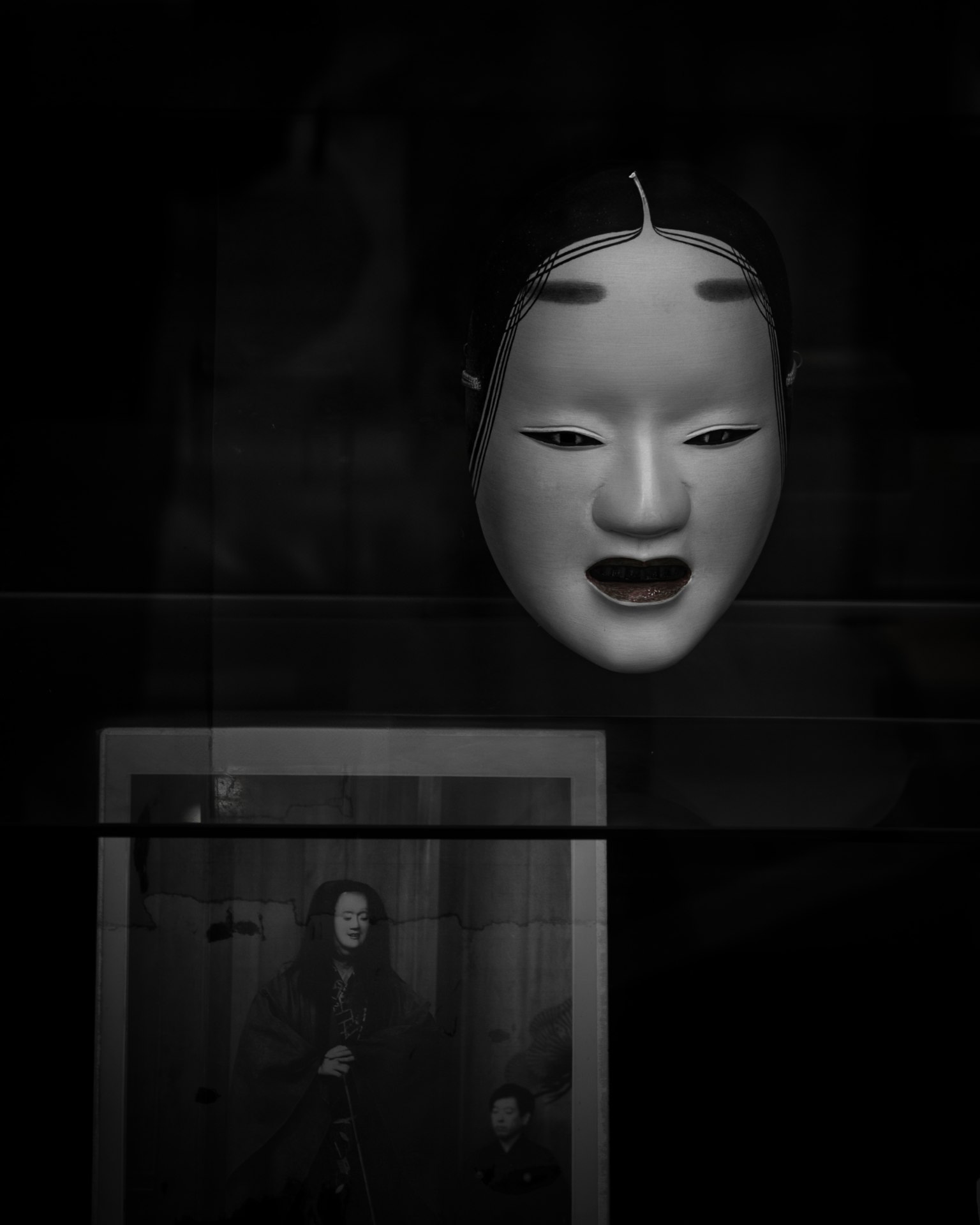 黒い背景に浮かぶ日本の伝統的な能面とその下に映る人物