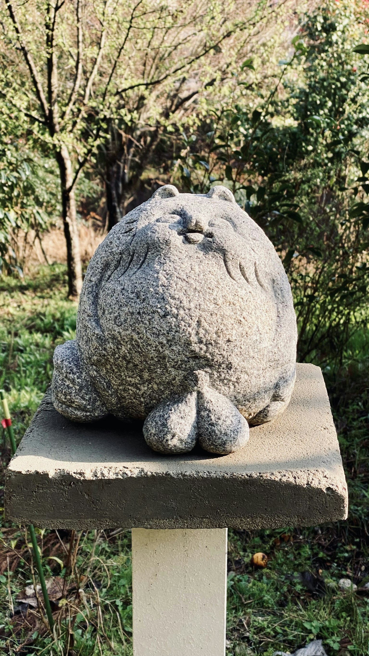 一座石制猫雕塑 resting在花园里的基座上