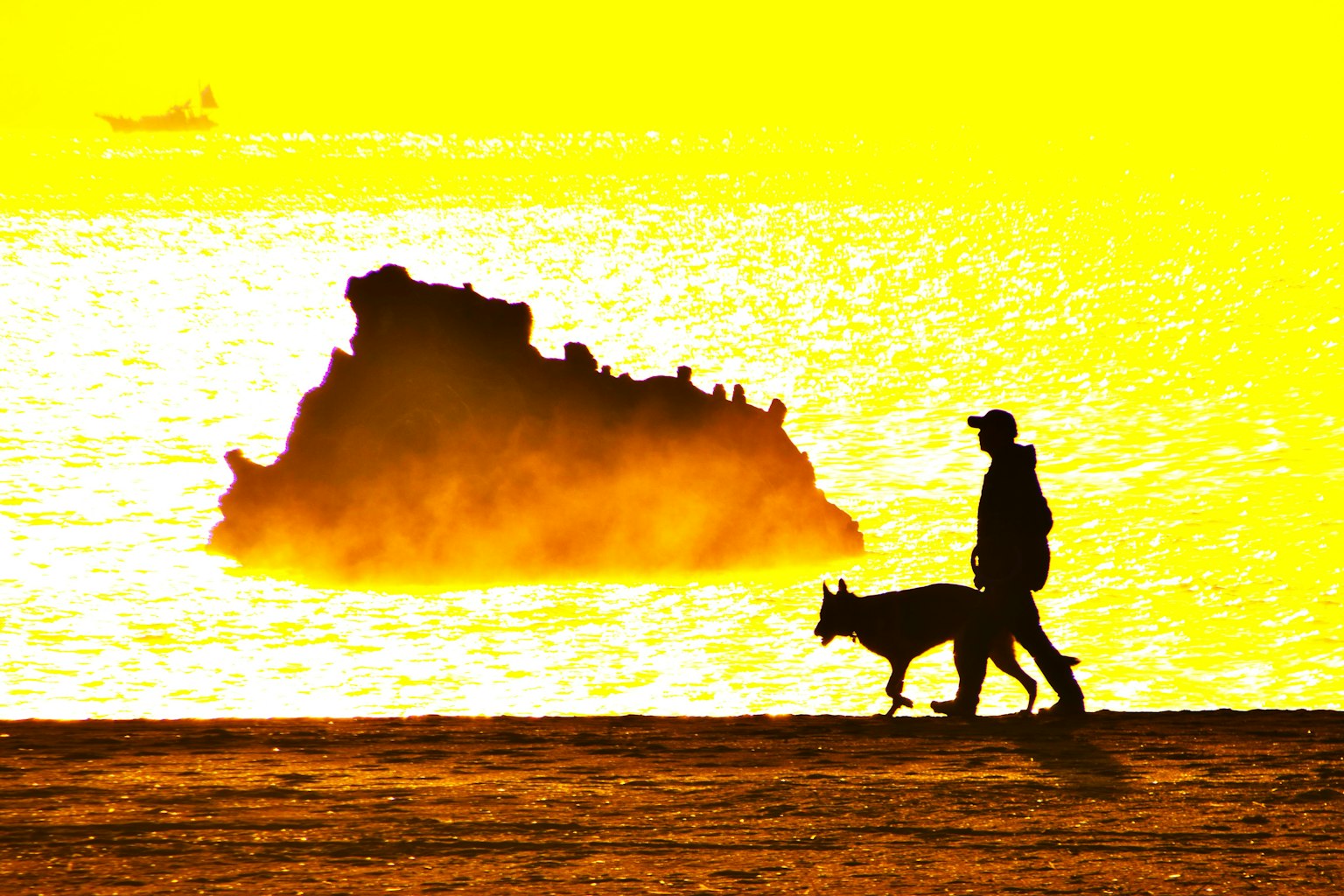 Silhouette di una persona che passeggia con un cane contro un tramonto sul mare con una roccia sullo sfondo