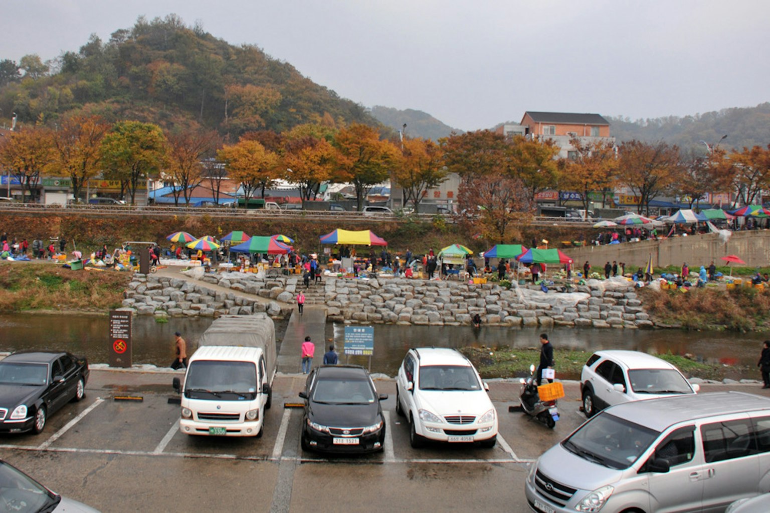 Area di parcheggio vicino a un fiume con tende colorate e alberi autunnali