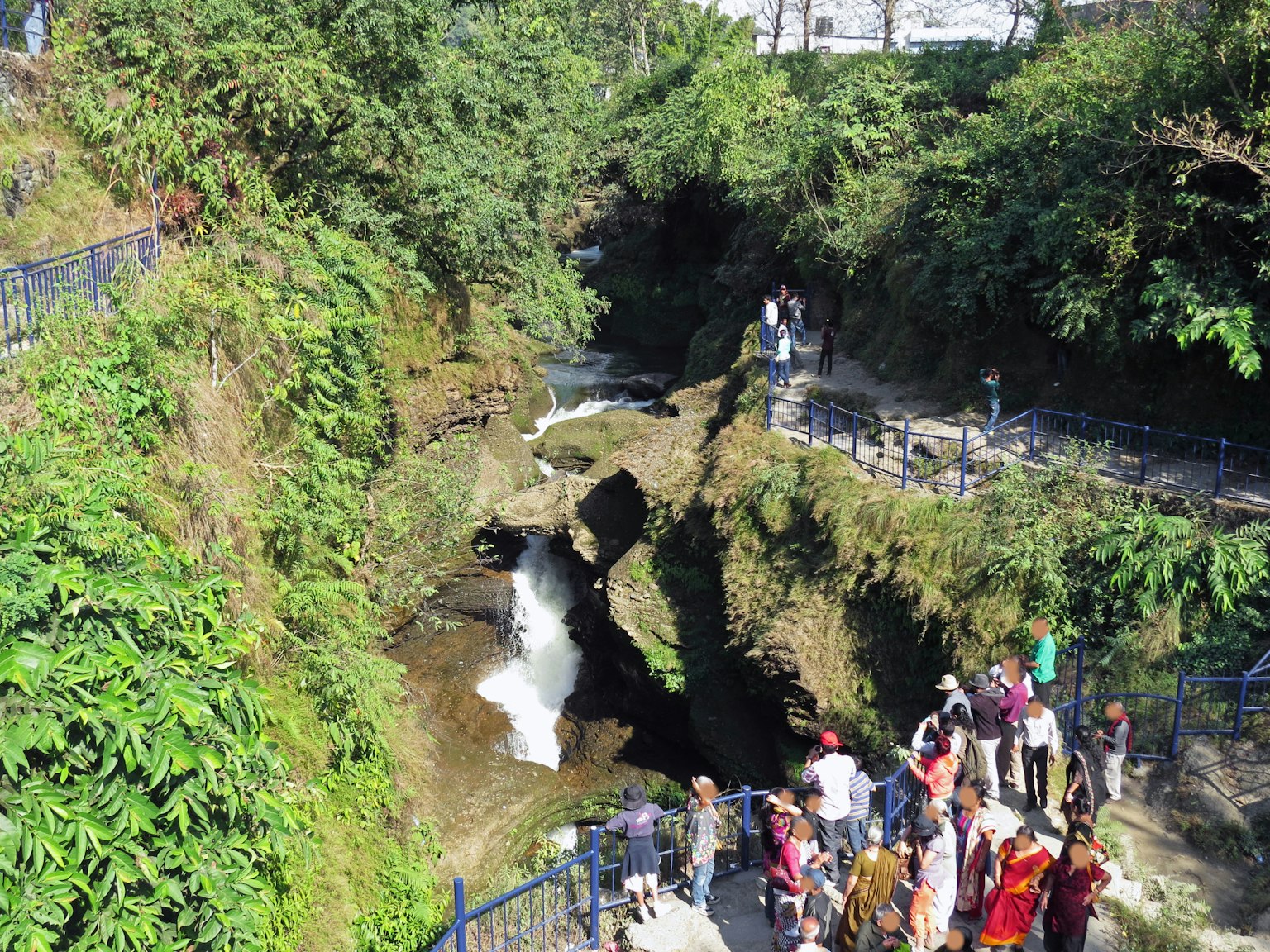 Wisatawan di dekat air terjun dengan vegetasi yang rimbun