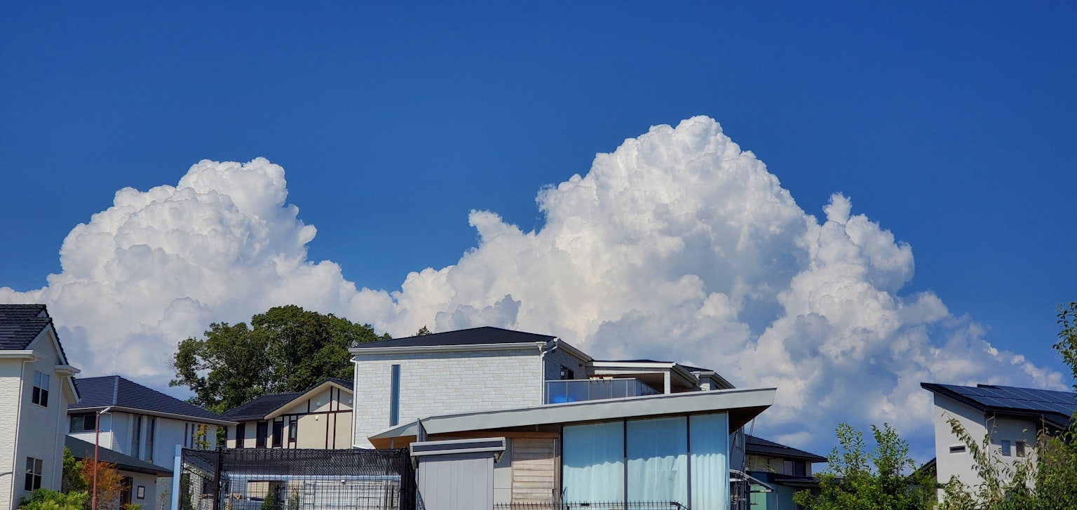 Pemandangan rumah modern di bawah langit biru dan awan putih berbulu