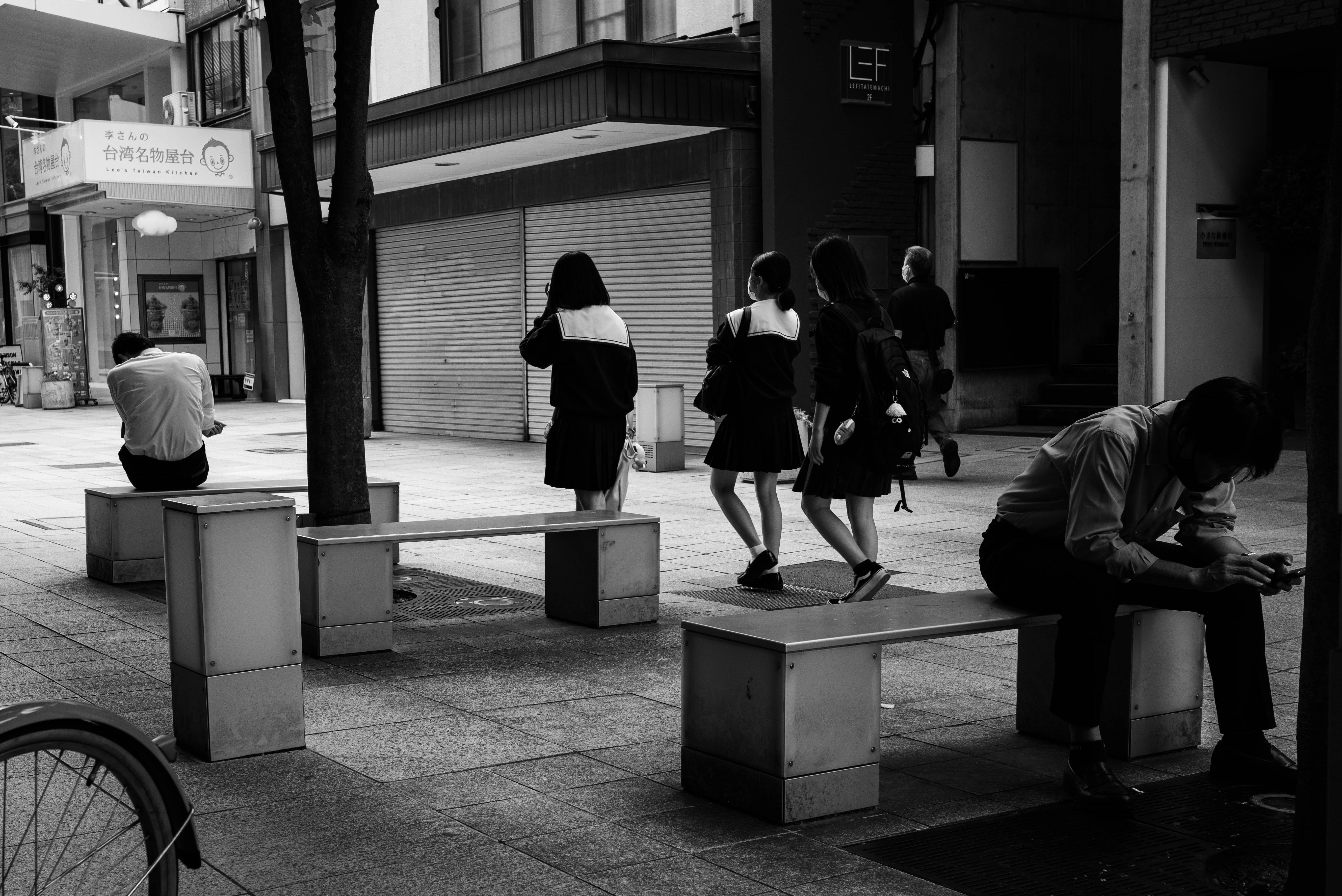 街中のベンチ前を歩く学生とサラリーマンのストリートスナップ