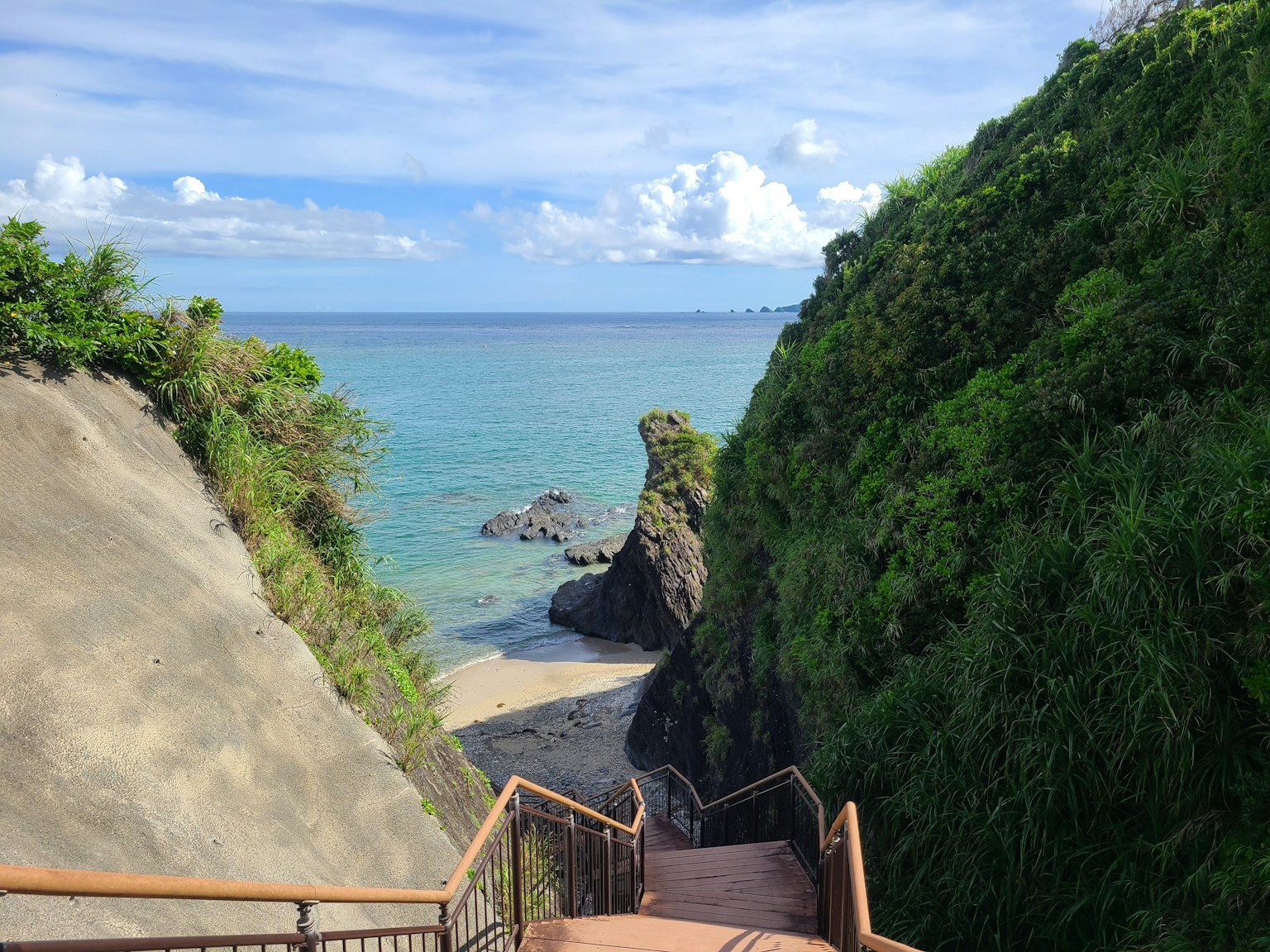 Pemandangan indah tangga menuju pantai yang dikelilingi tebing hijau dan langit biru