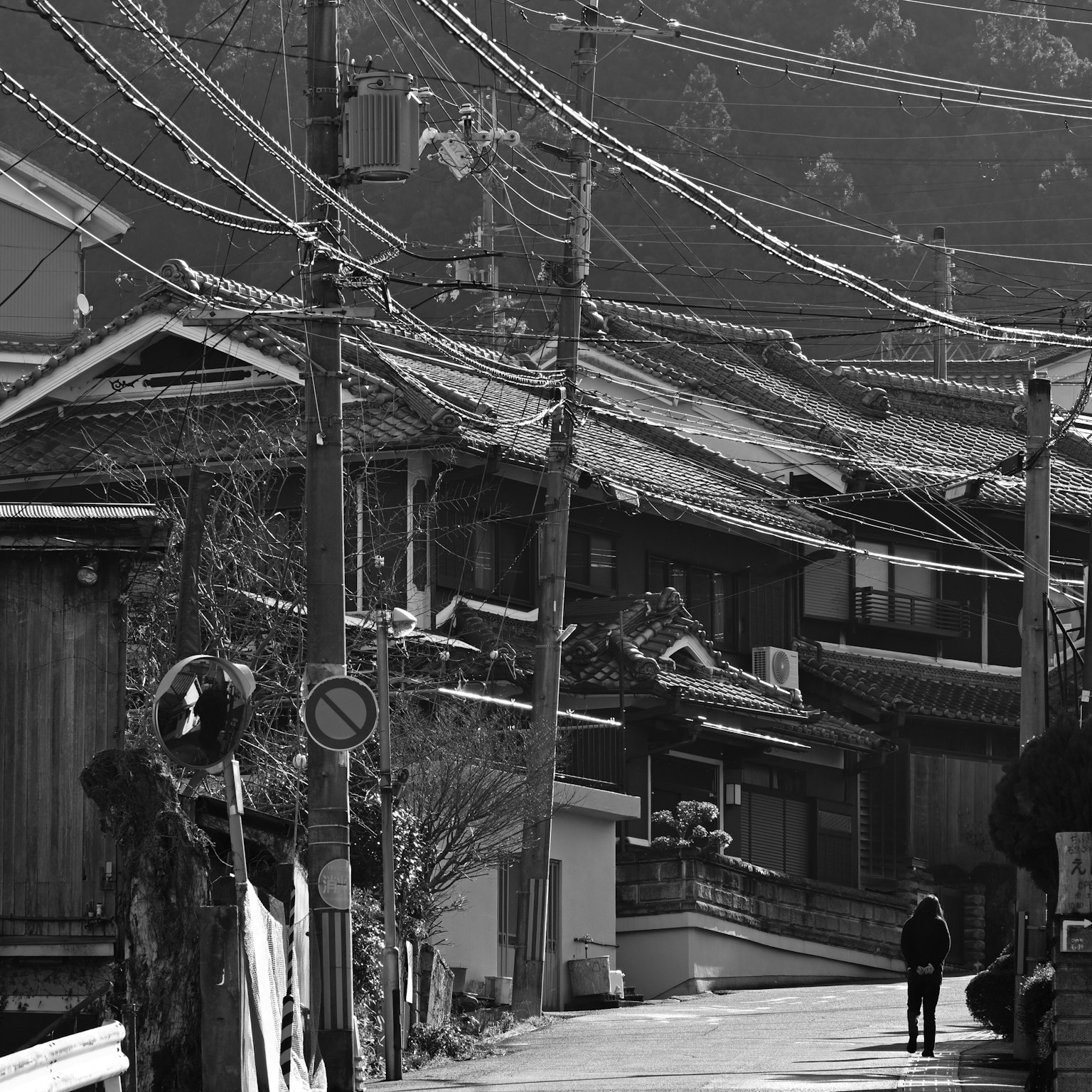 Escena tranquila de un pueblo japonés con casas antiguas y una persona caminando por una calle cruzada por líneas eléctricas