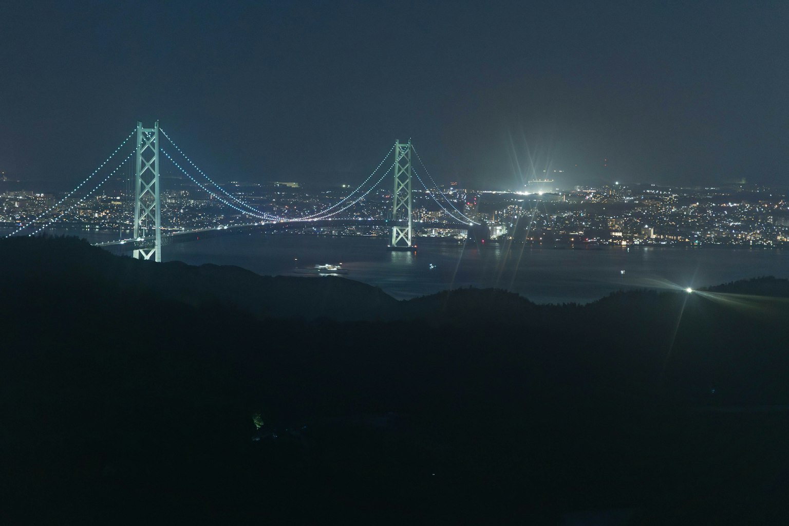 Nachtansicht der Akashi-Kaikyō-Brücke mit Stadtlichtern im Hintergrund