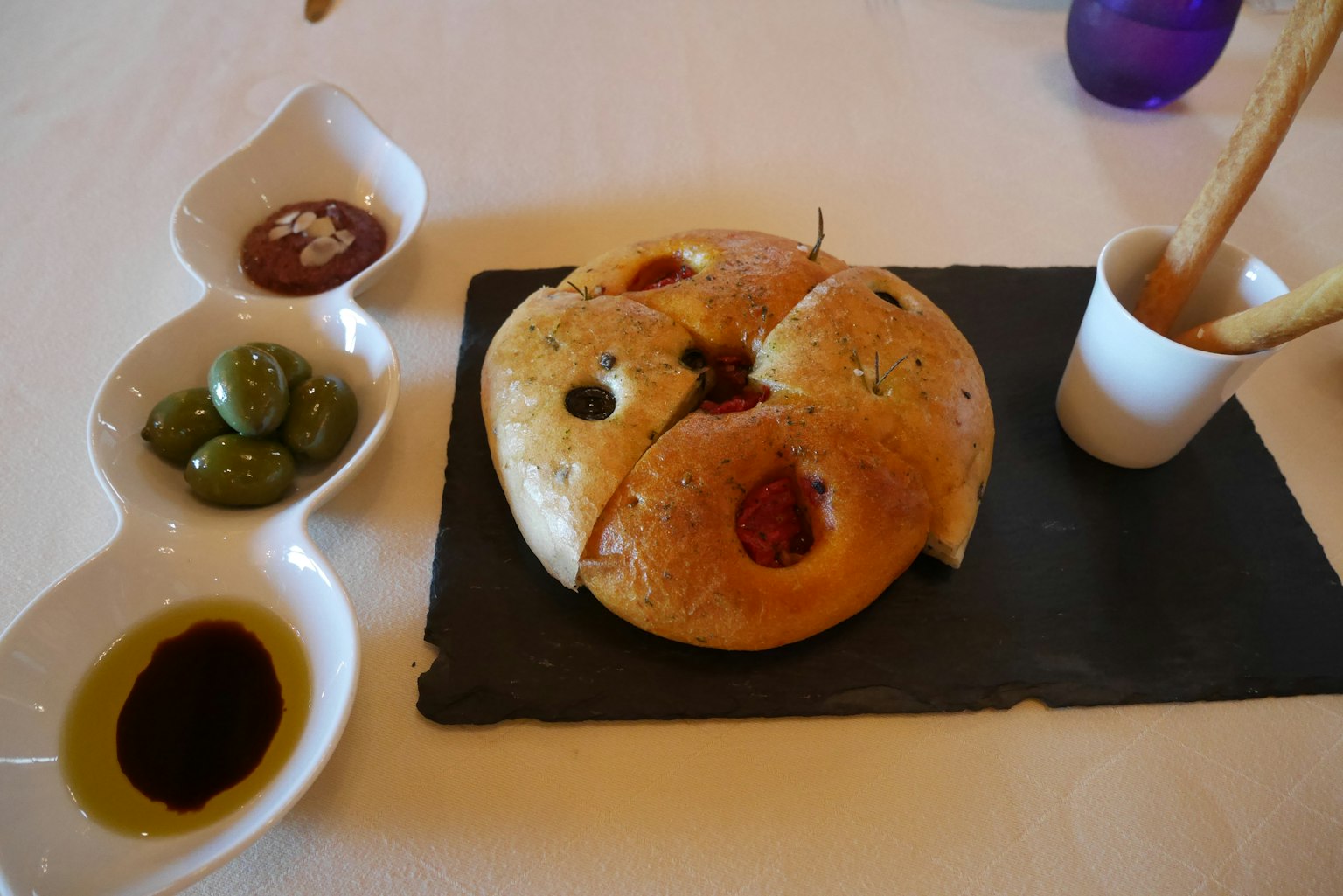 A round bread with olives and dipping sauces presented on a slate plate