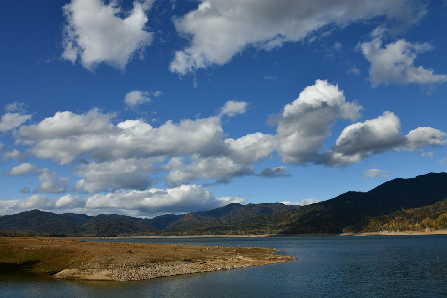 Vue pittoresque d'un lac bleu entouré de montagnes et de nuages blancs moelleux