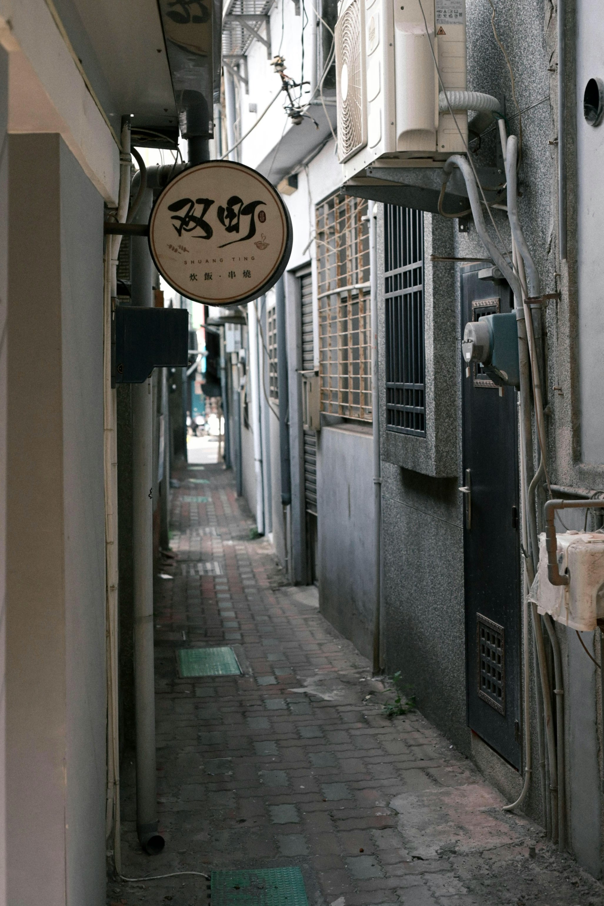 路地の壁に掛かった丸い看板のある狭い通り