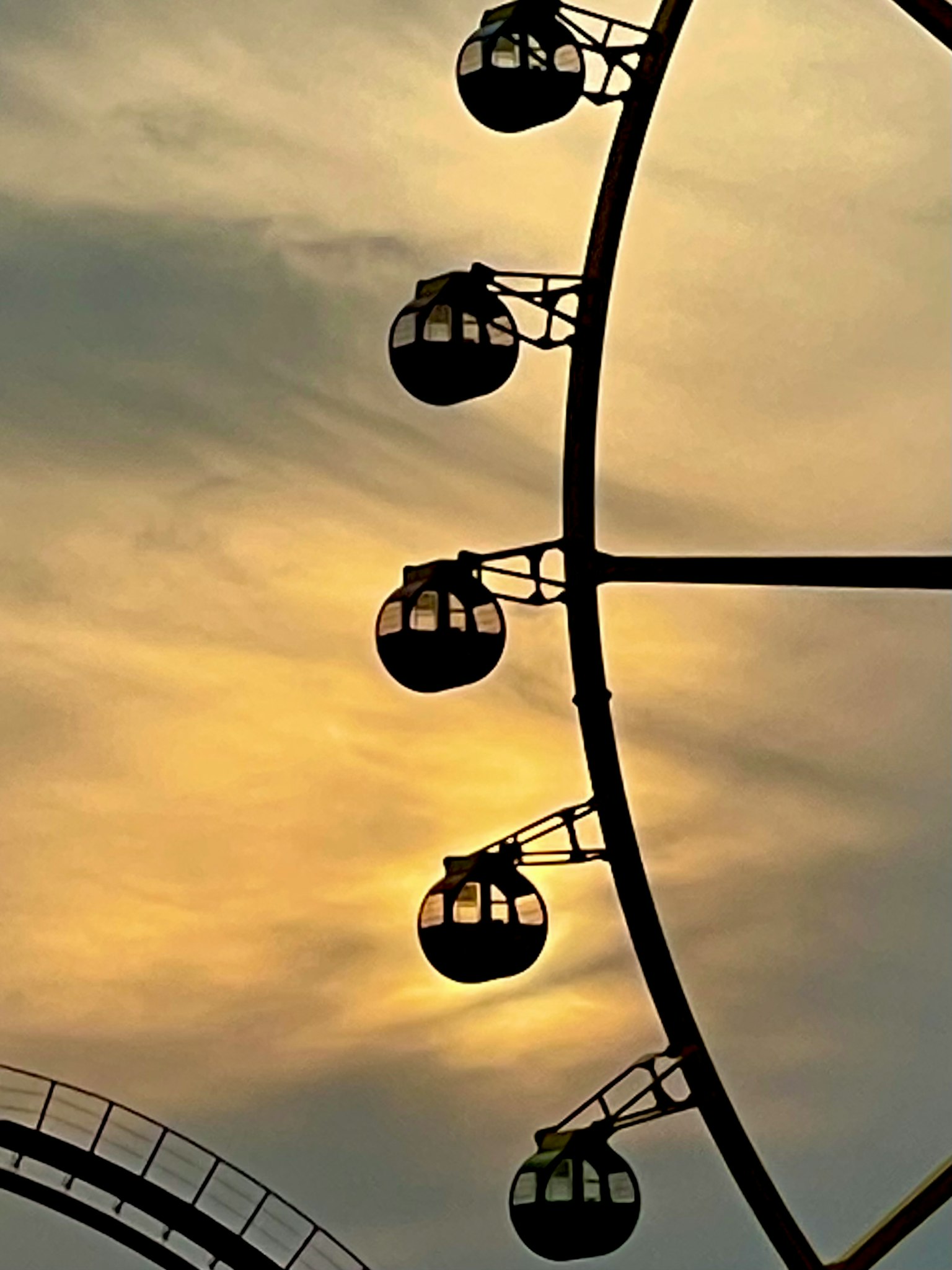 Silhouette of a Ferris wheel with gondolas against a sunset sky