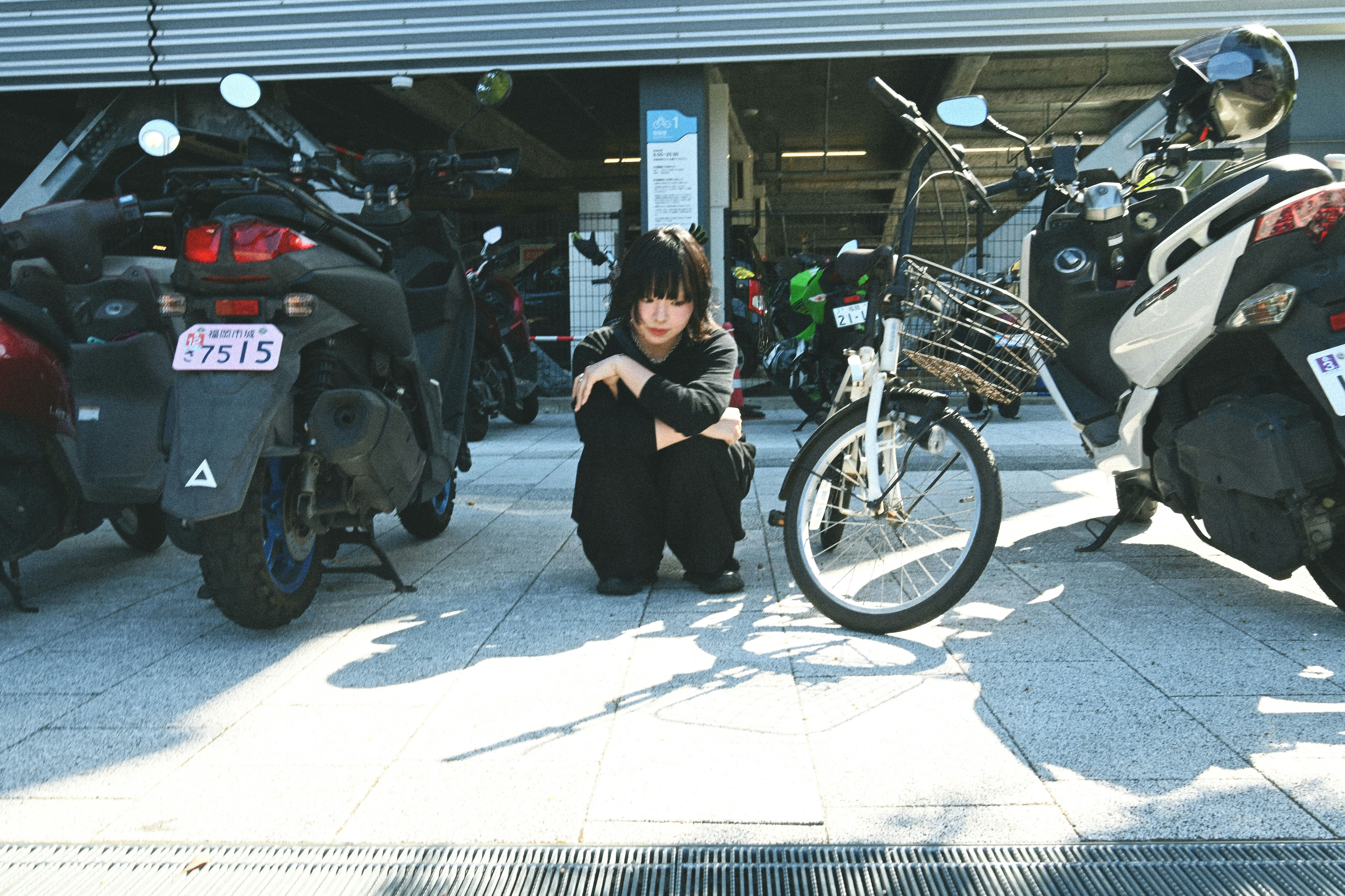 バイクと自転車が並ぶ屋外の駐輪スペースで立つ女性
