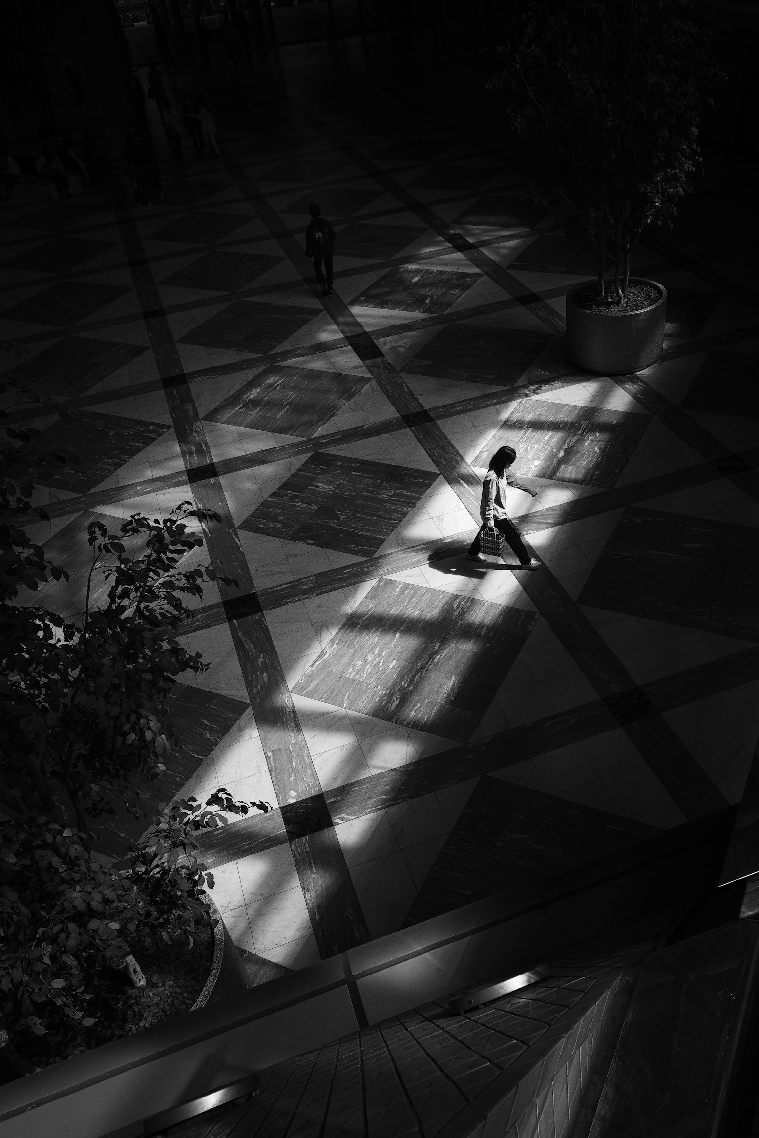 Seseorang berdiri di ruang hitam putih dengan kontras tinggi dan pola cahaya yang mencolok