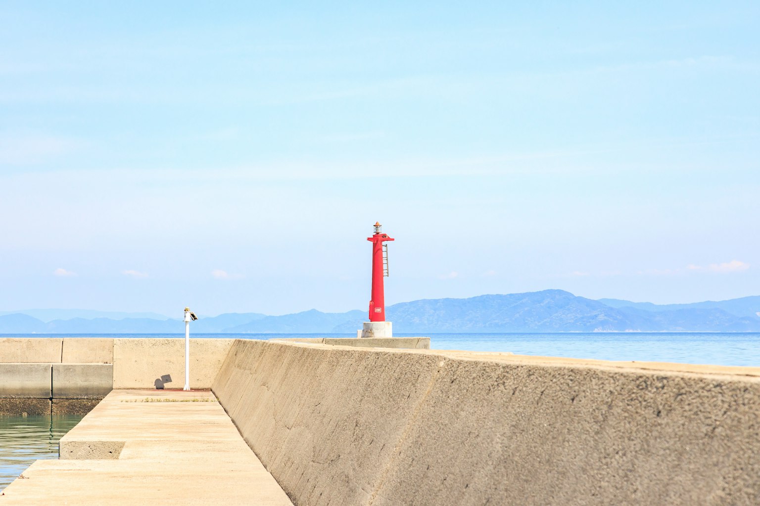 Un phare rouge se dresse sur une jetée face à la mer