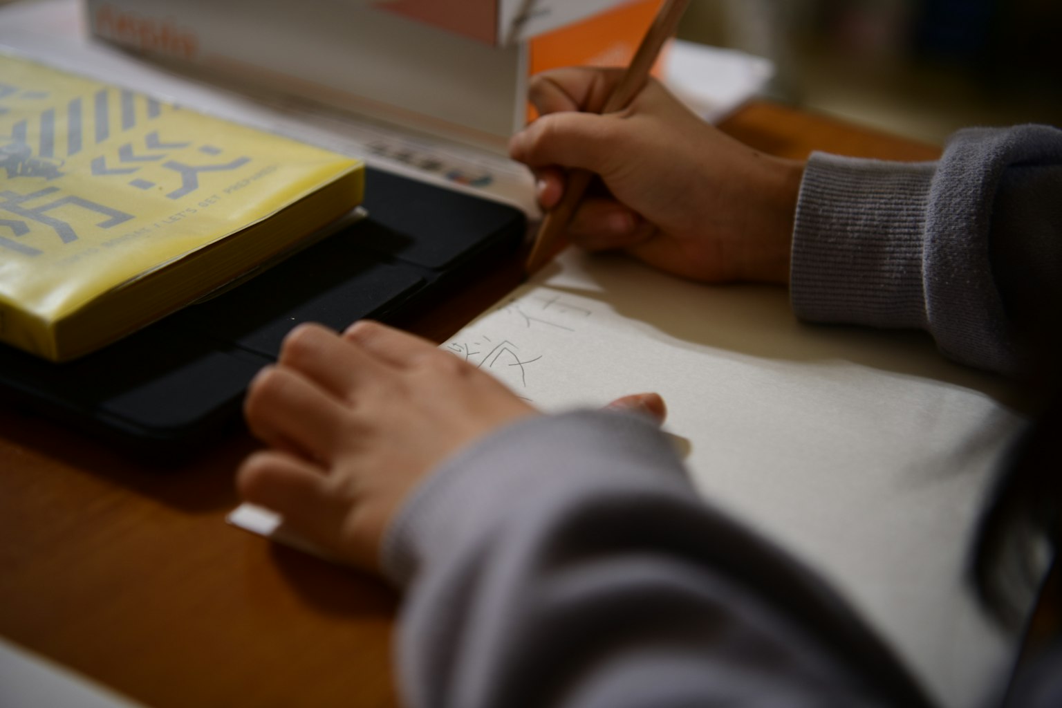 Mains écrivant dans un carnet sur une table avec un livre jaune à proximité