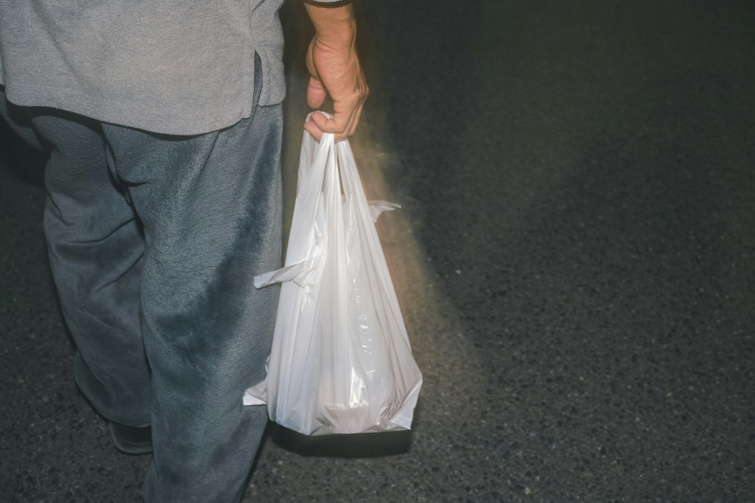 어두운 도로를 걷고 있는 흰색 비닐봉지를 들고 있는 사람