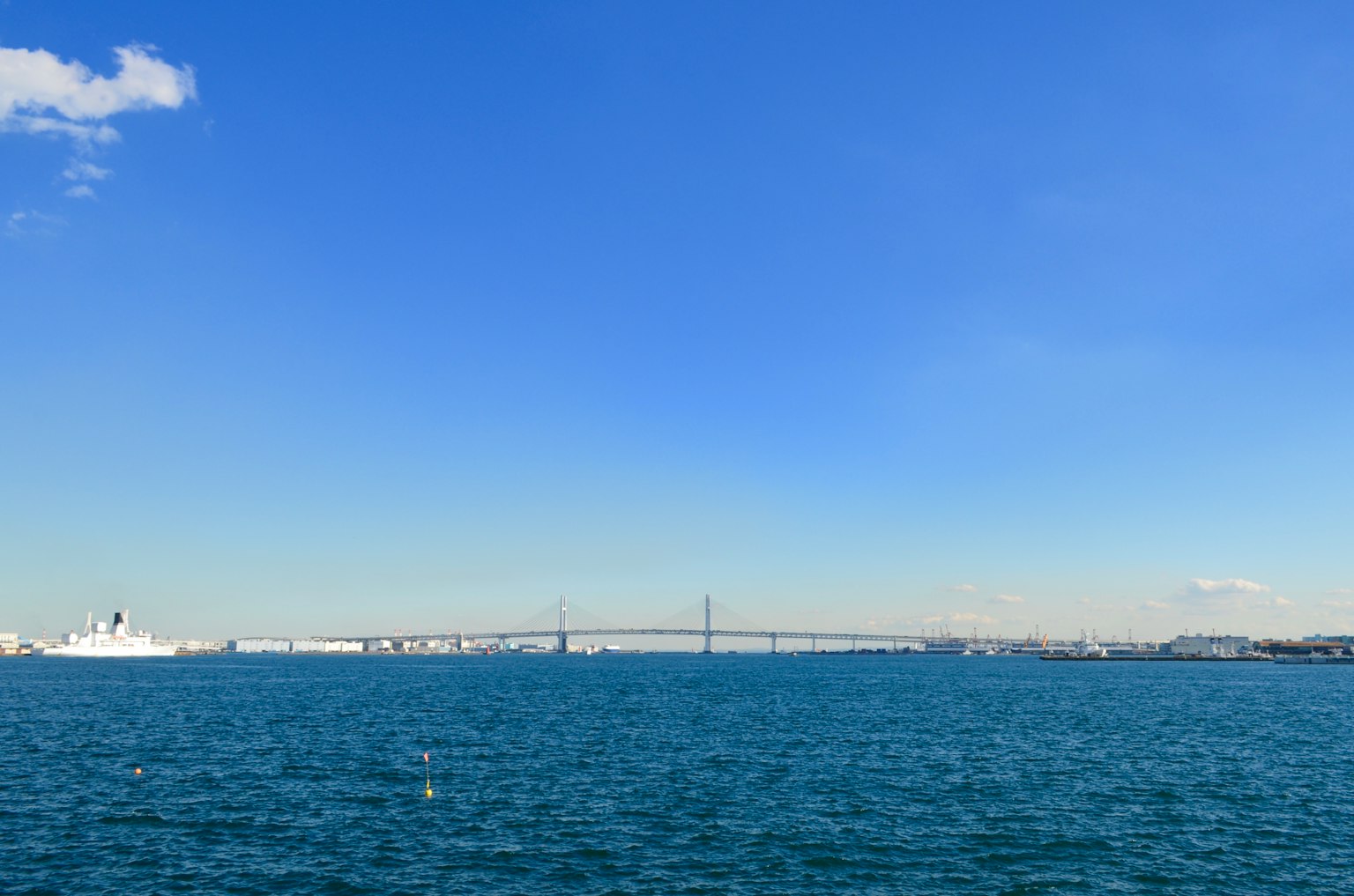 在晴朗的蓝天下和宁静的海面上，有一座桥和船只的风景