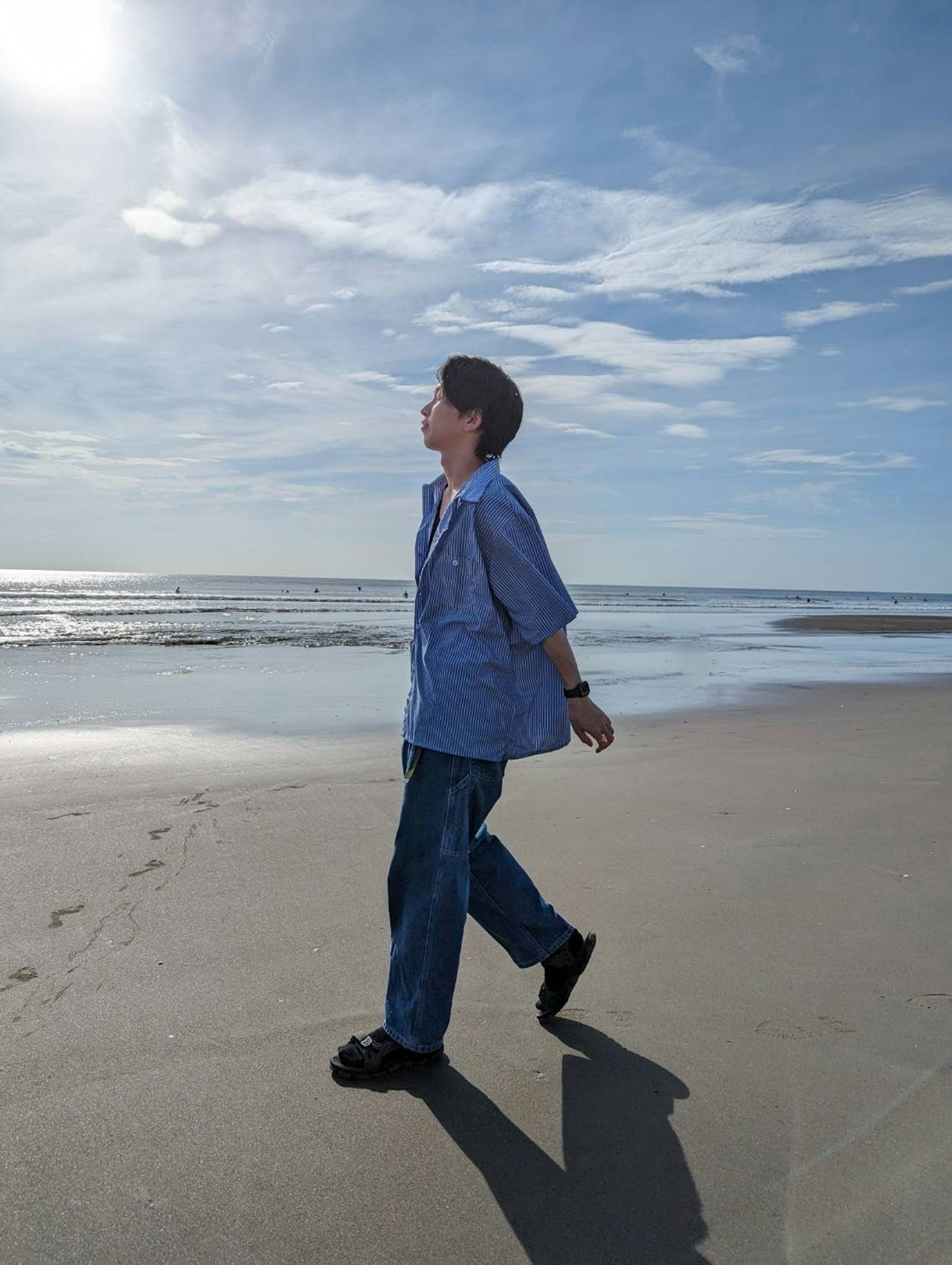 Un hombre caminando por la playa con cielo azul y océano de fondo