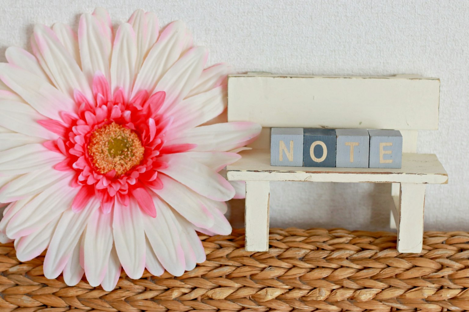 Un pequeño banco blanco con letras en bloque que dicen NOTE y una gran flor rosa al lado