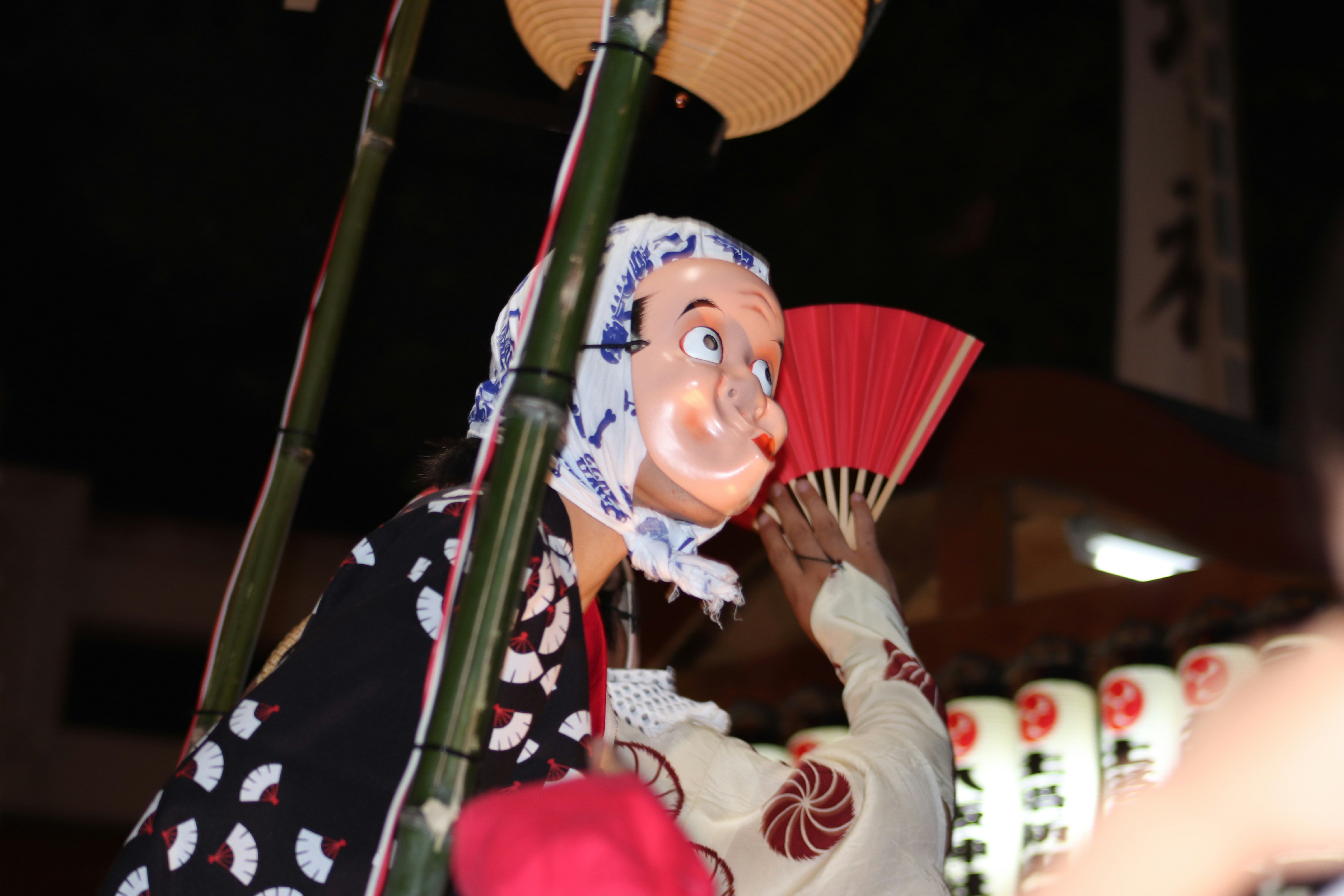 Japanese doll in traditional attire holding a fan in front of bamboo
