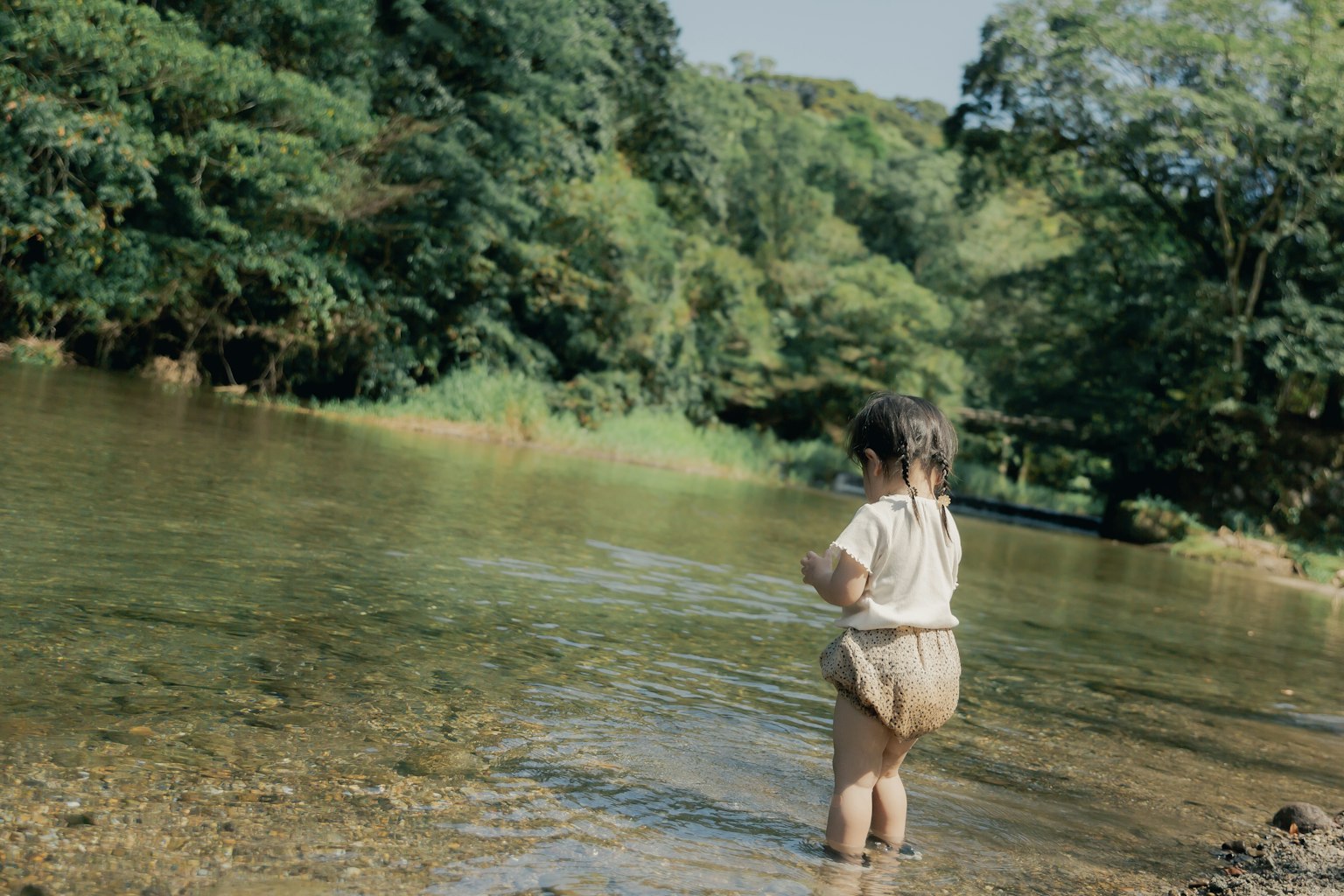 Tout-petit jouant au bord de la rivière entouré de verdure luxuriante