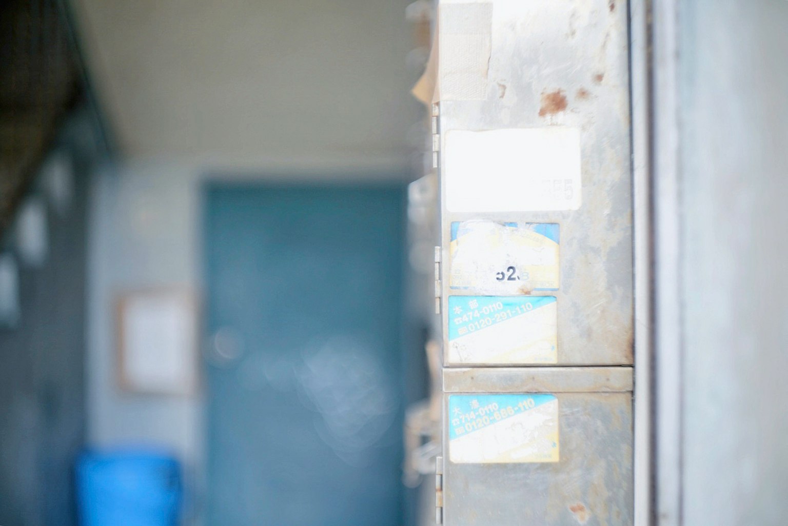 Un couloir avec des anciennes boîtes aux lettres une porte bleue et une poubelle bleue en arrière-plan