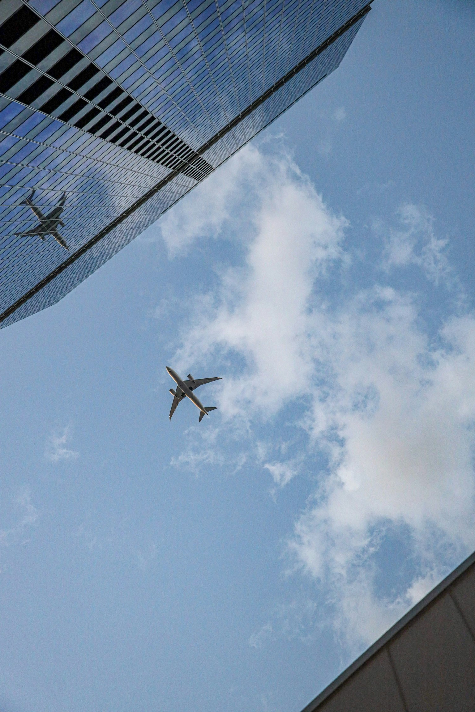 An airplane flying against a blue sky with reflections from a skyscraper