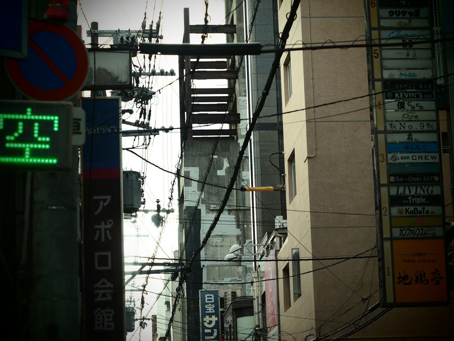 Städtische Szene mit Stromleitungen und Gebäuden mit grünem Schild und japanischem Text