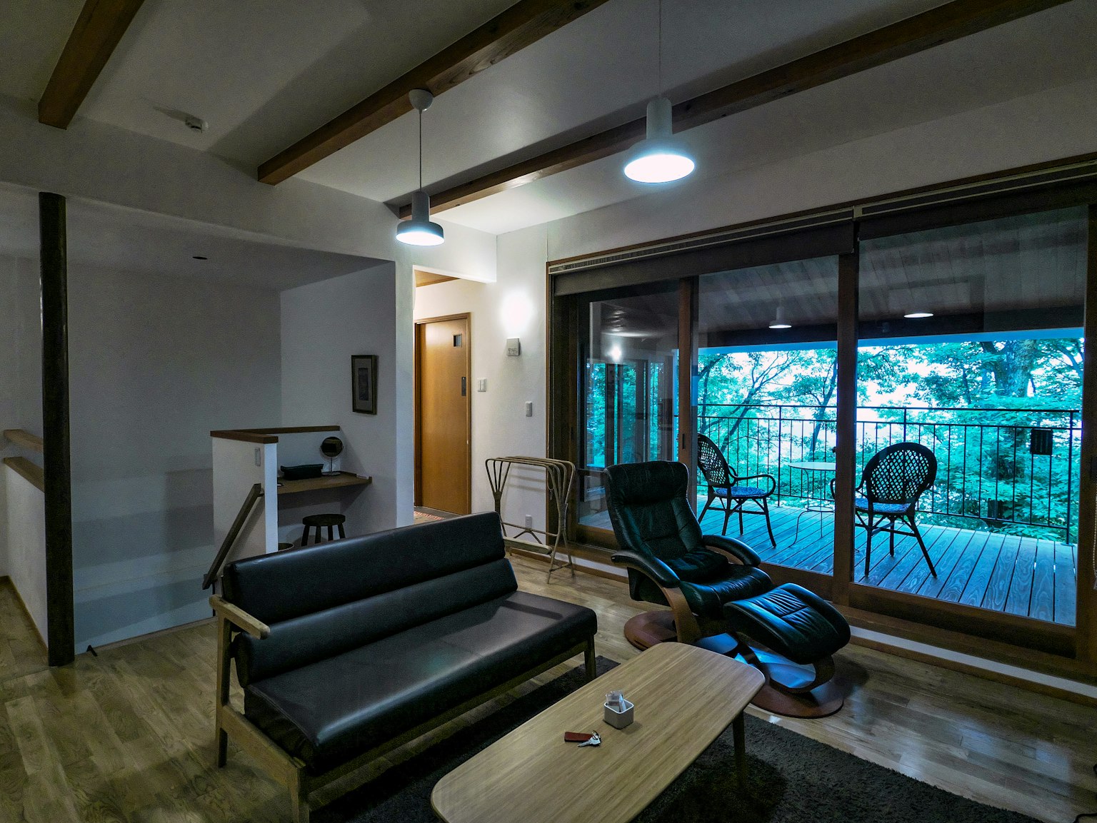 Modernes Wohnzimmerinterieur mit schwarzem Sofa zwei Stühlen und einem Couchtisch mit großem Fenster, das eine grüne Aussicht zeigt