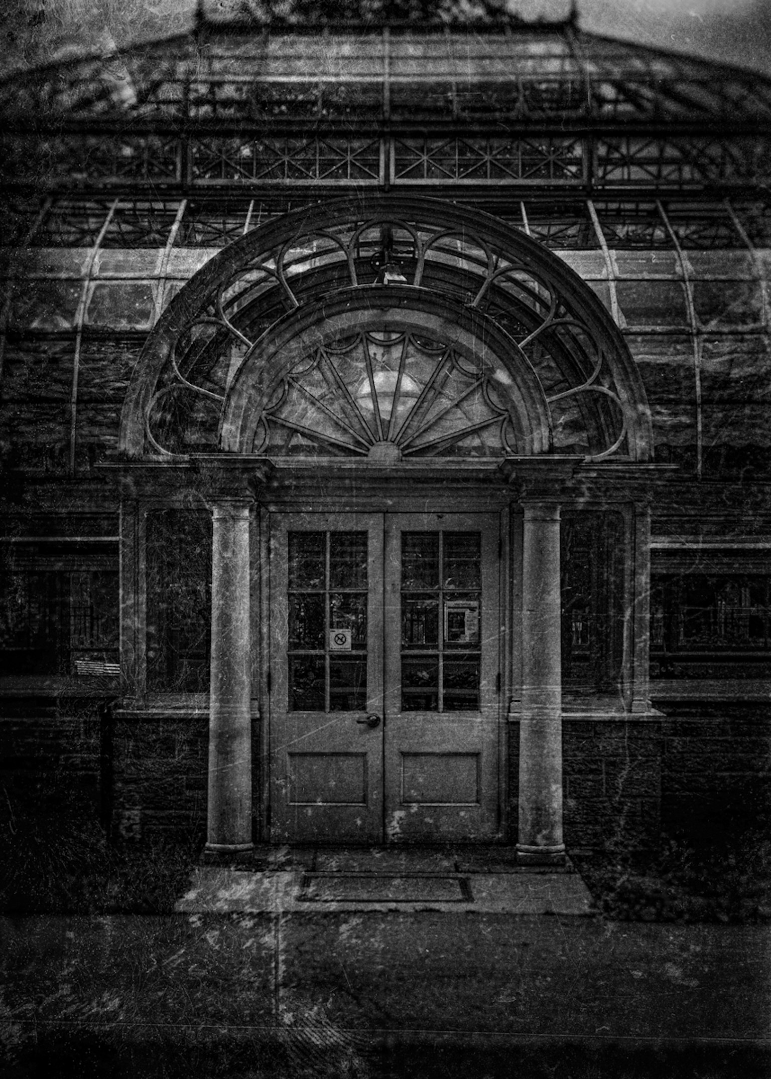 오래된 온실 입구의 흑백 사진 섬세한 유리 아치와 나무 문이 특징