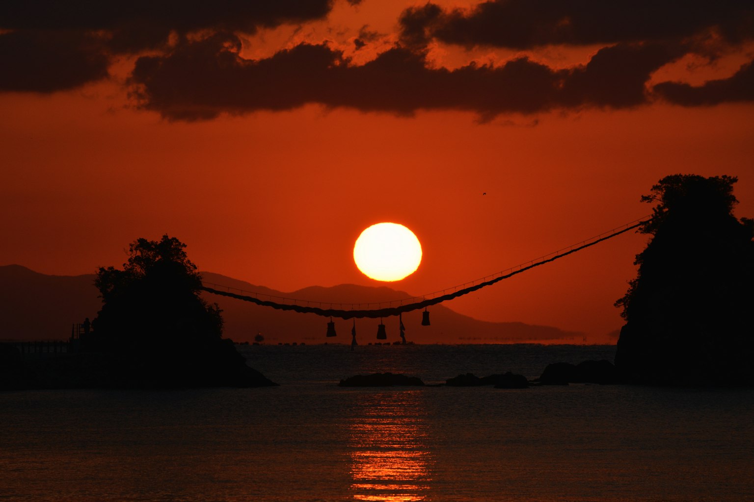 Un impresionante atardecer con un cielo naranja sobre el mar luces colgantes de un puente