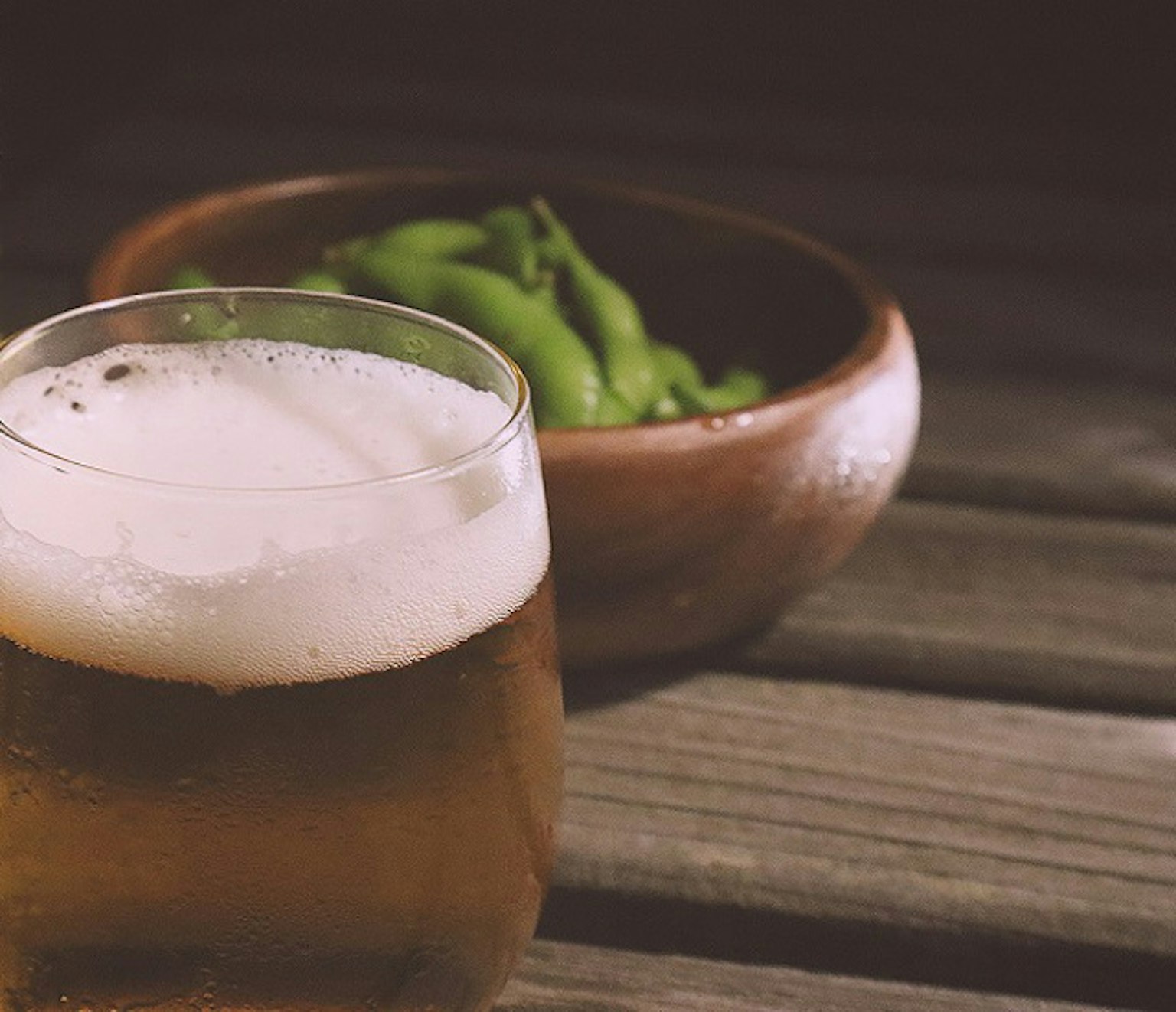 Một ly bia và một bát đậu edamame trên bàn gỗ