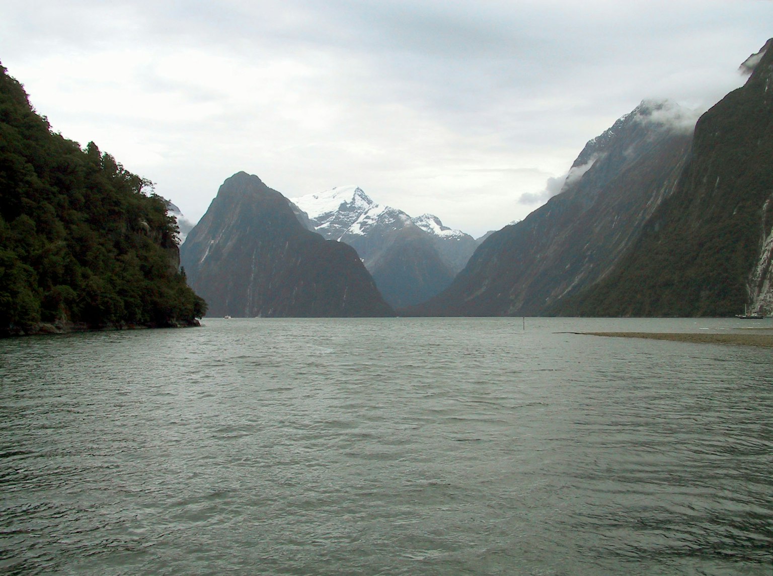 Vue pittoresque d'une eau calme entourée de montagnes majestueuses avec un ciel nuageux et des sommets enneigés
