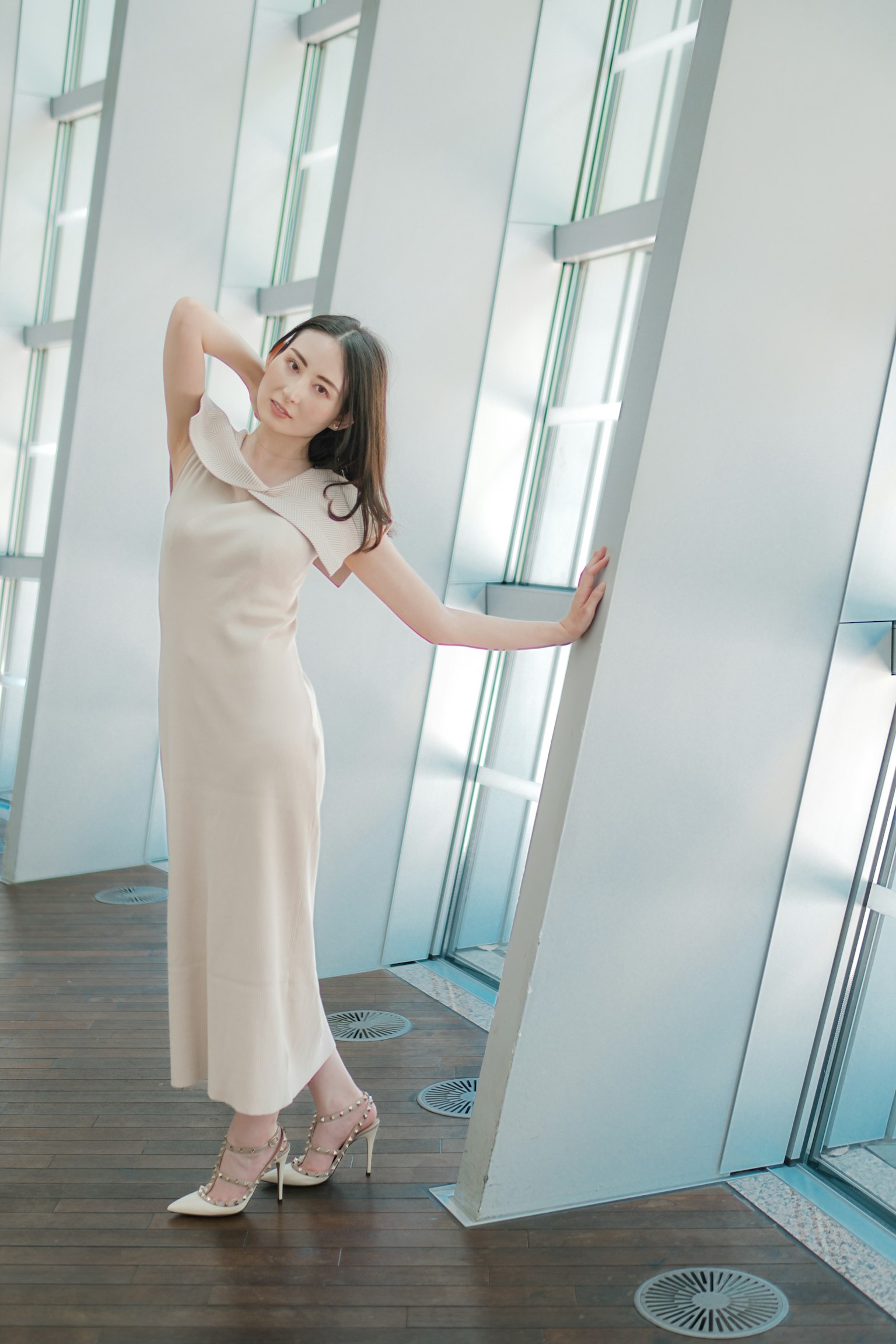 Eine Frau, die in einem einfachen beigen Kleid in einem modernen Gebäude posiert