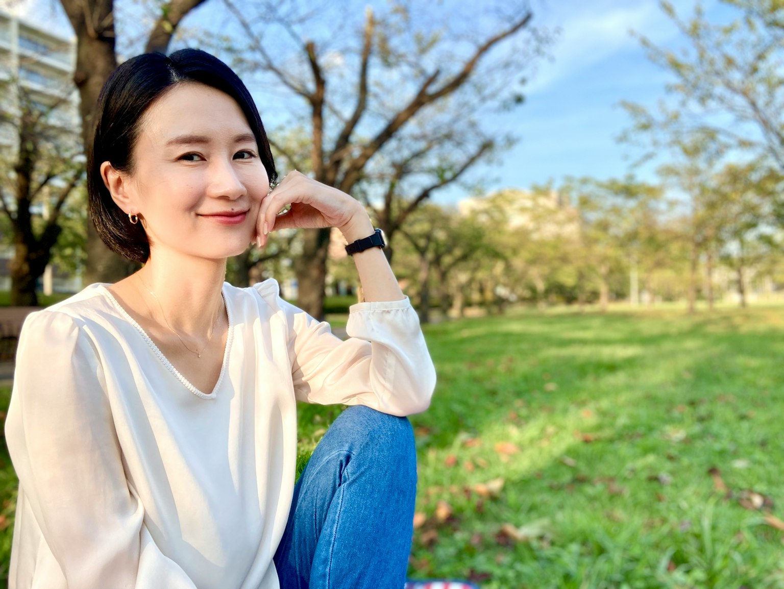 公園裡微笑的女性穿著白色上衣和藍色牛仔褲綠色草坪和樹木背景