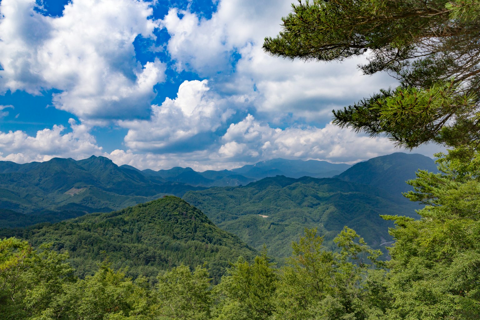 Montagne verdi con nuvole espanse in un cielo blu chiaro
