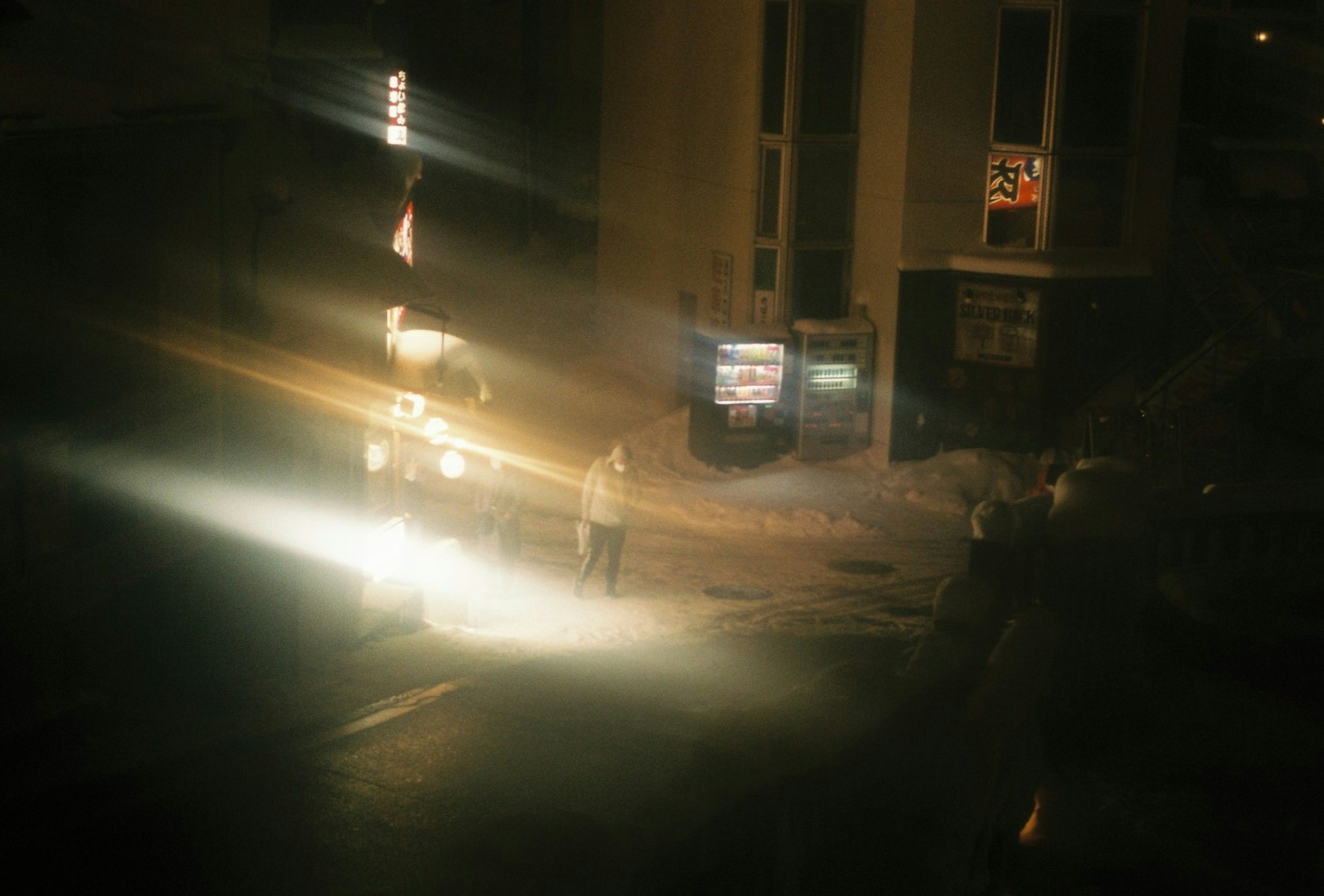 Foto di una strada poco illuminata di notte con silhouette di persone