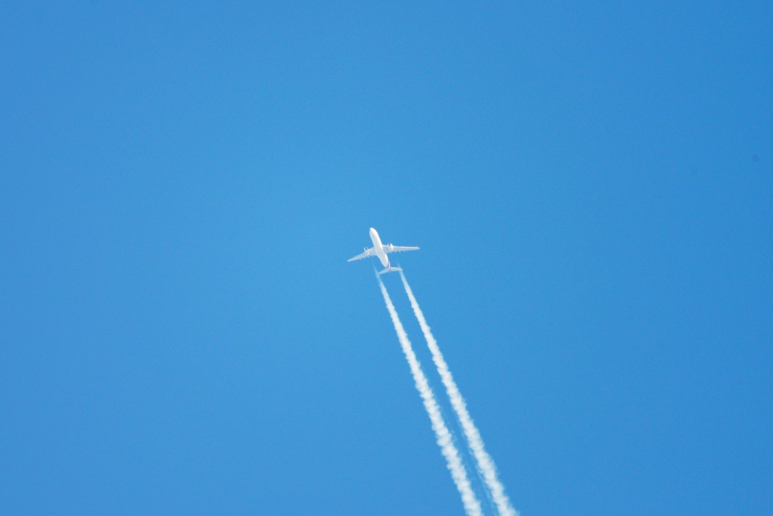 Ein Flugzeug fliegt in einem klaren blauen Himmel und hinterlässt weiße Kondensstreifen